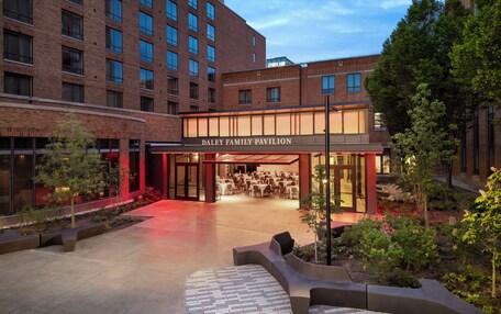 A hotel entrance with a covered outdoor seating area, a brick facade, and a landscaped garden.