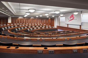 A conference room with tiered seating, wooden paneling, and a large screen displaying 'The Blackwell' logo.