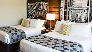 A hotel room with two beds, a fireplace, a lamp, and a large window with a view of a building.