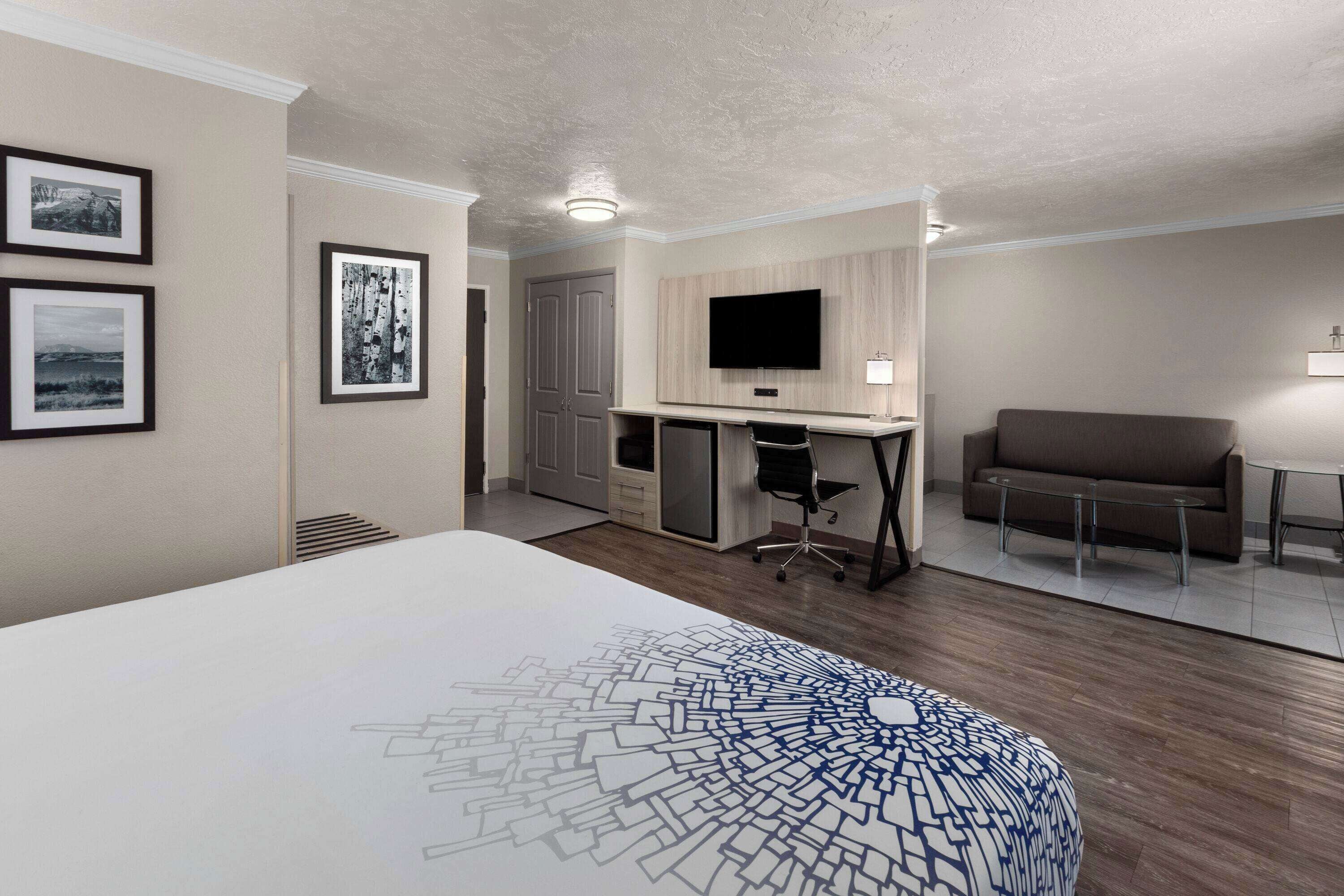A modern hotel room with a large bed, a desk with a computer, a TV, and a sofa.