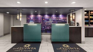 A hotel reception area with two reception desks, a cityscape mural, and a self-service kiosk. - La Quinta Inn & Suites by Wyndham North Orem (Orem)