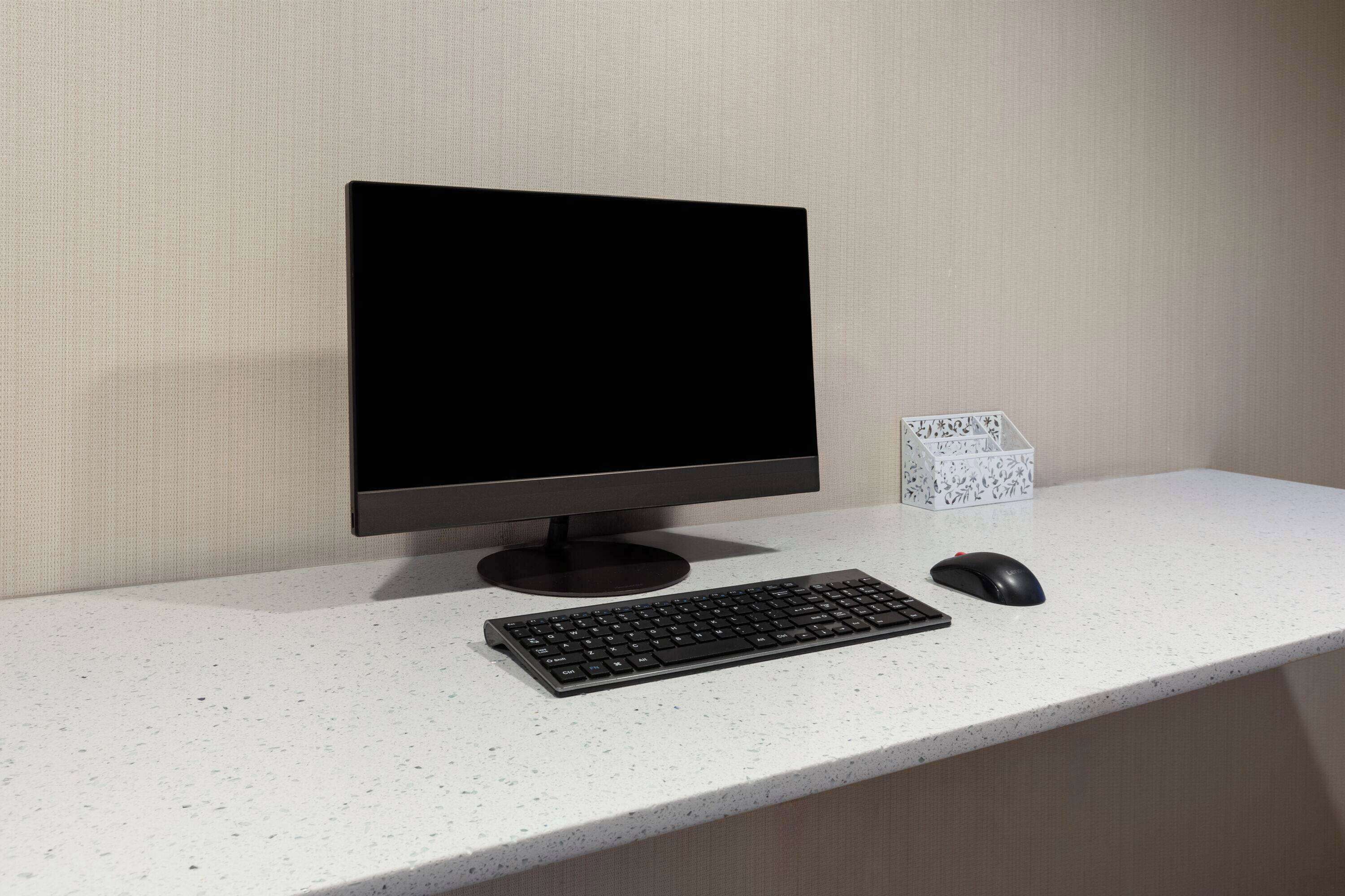 Un espacio de trabajo moderno con una computadora de escritorio, teclado y ratón sobre un escritorio blanco con motas, frente a una pared con textura.
