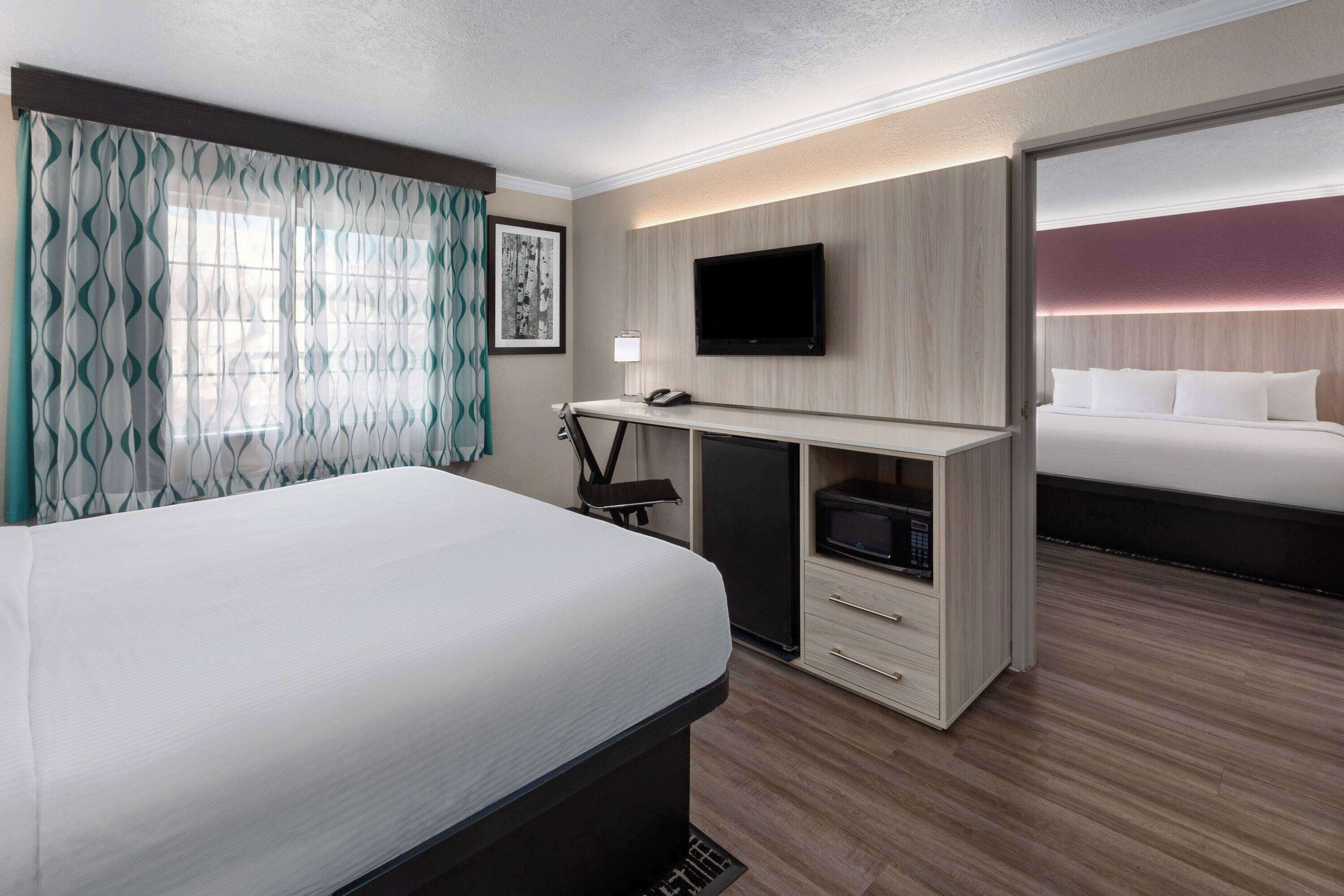 A hotel room with a large bed, a desk with a flat-screen TV, a microwave, and a small refrigerator.