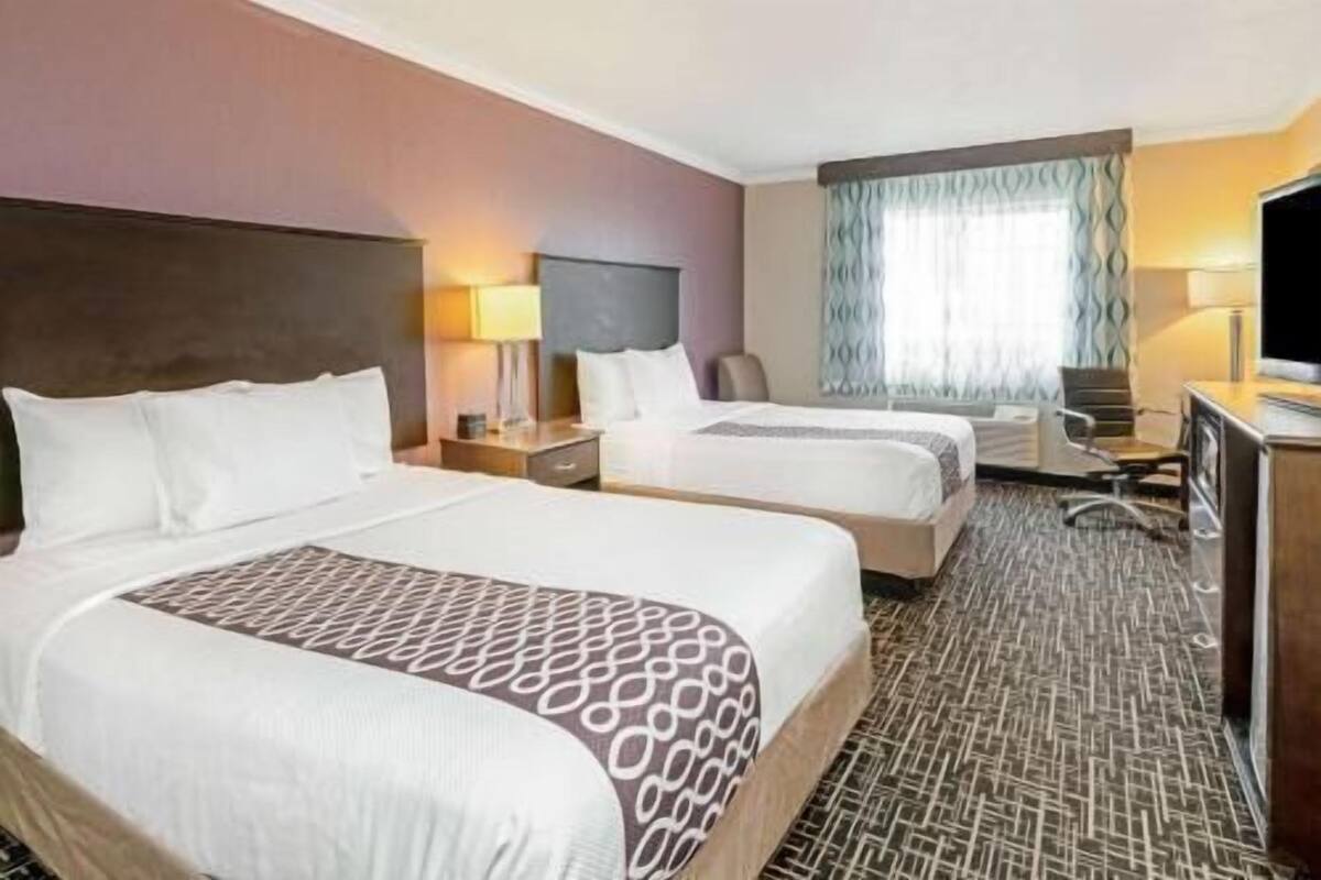 A hotel room with two beds, a desk, a chair, and a television.