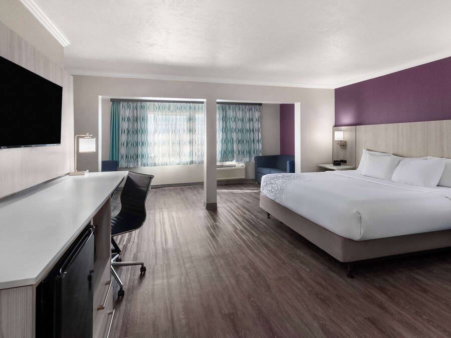Habitación de hotel con cama, escritorio, silla, televisor y ventana con cortinas.