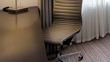 Un fauteuil de bureau moderne, doté d’un haut dossier et d’accoudoirs, placé à côté d’un bureau sur lequel se trouve une lampe.