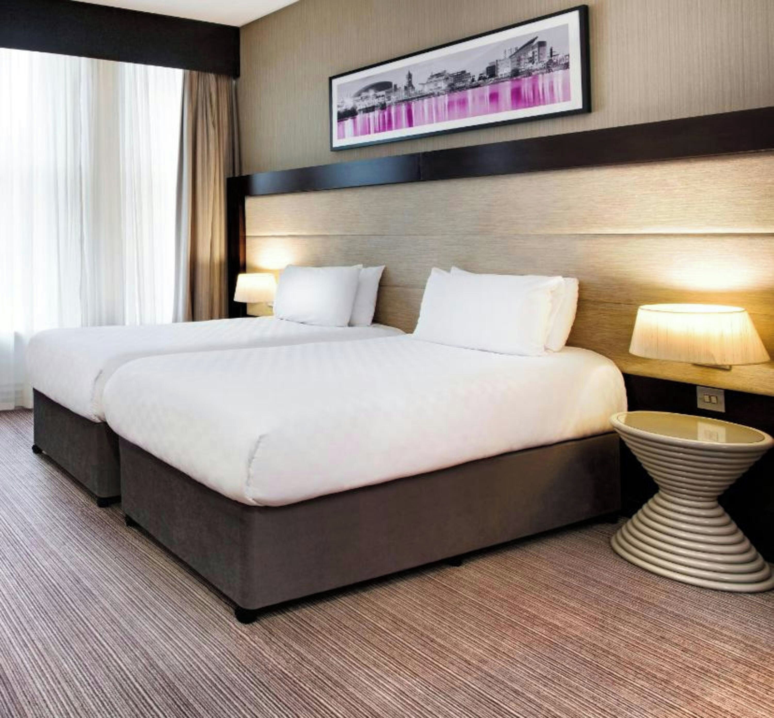 A hotel room with a double bed, two bedside tables, a headboard, and a framed picture on the wall.