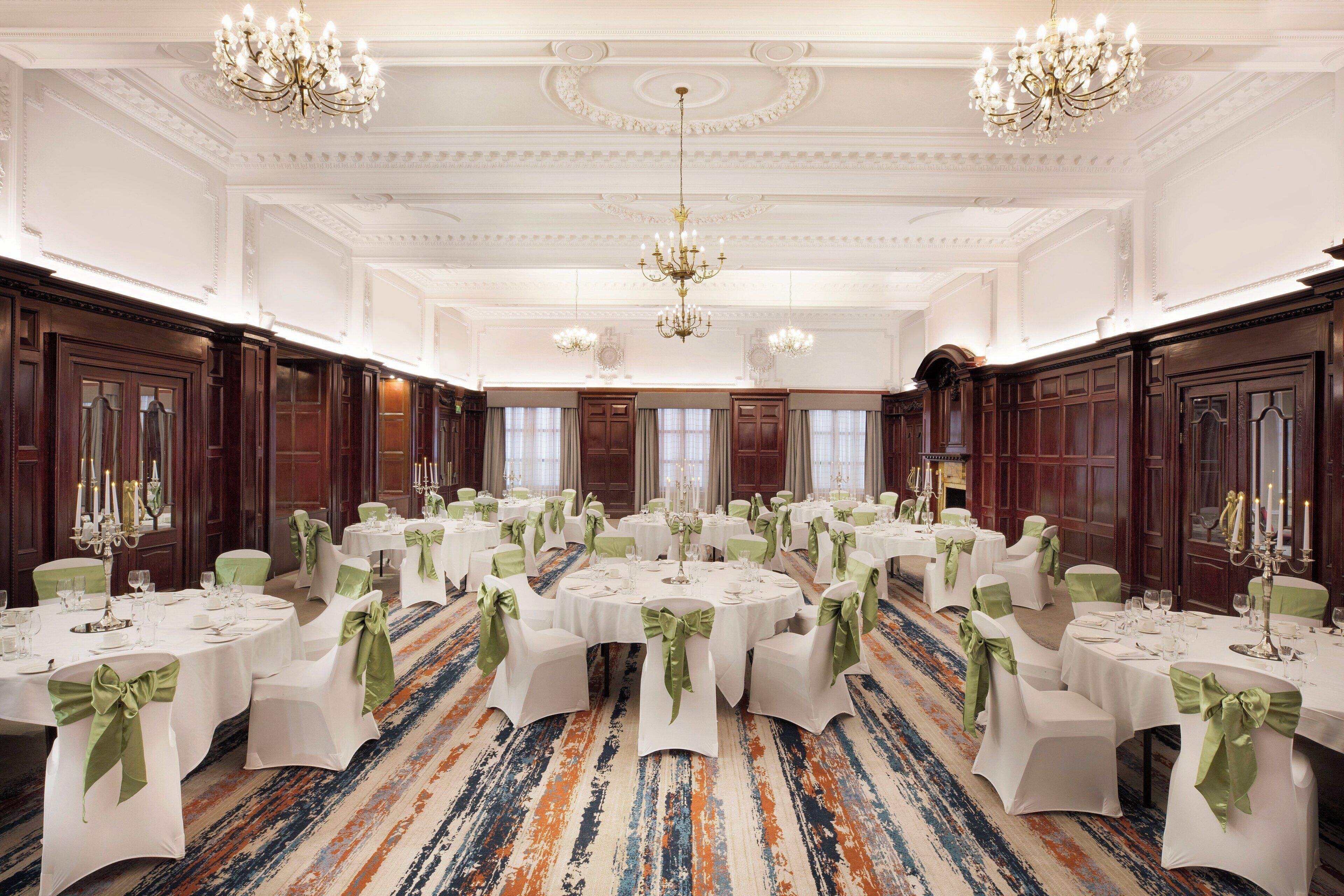 A banquet hall with round tables, white tablecloths, and green sashes.