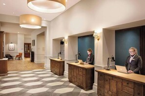A hotel lobby with reception desks, a check-in counter, and a seating area with chairs.