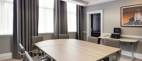 A conference room with a large table, chairs, a carpeted floor, and a painting of a castle on the wall.