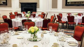 A banquet hall with round tables set for dining, red upholstered chairs, and a fireplace in the background.