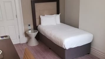 A hotel room with a bed, a bedside table, a chair, a round table, a framed picture on the wall, and a door.