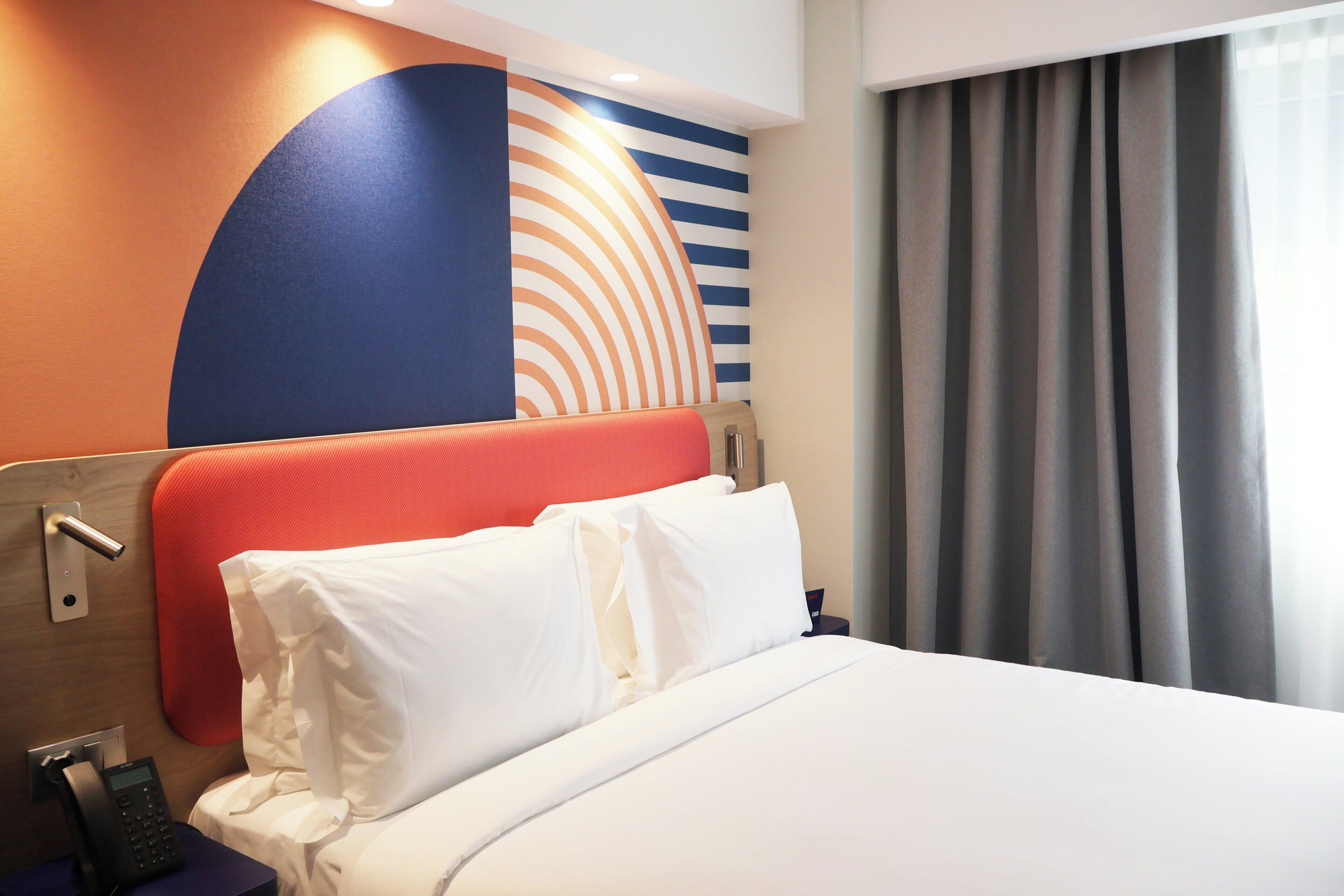 A hotel room with a bed, a telephone, and a wall with a geometric design.