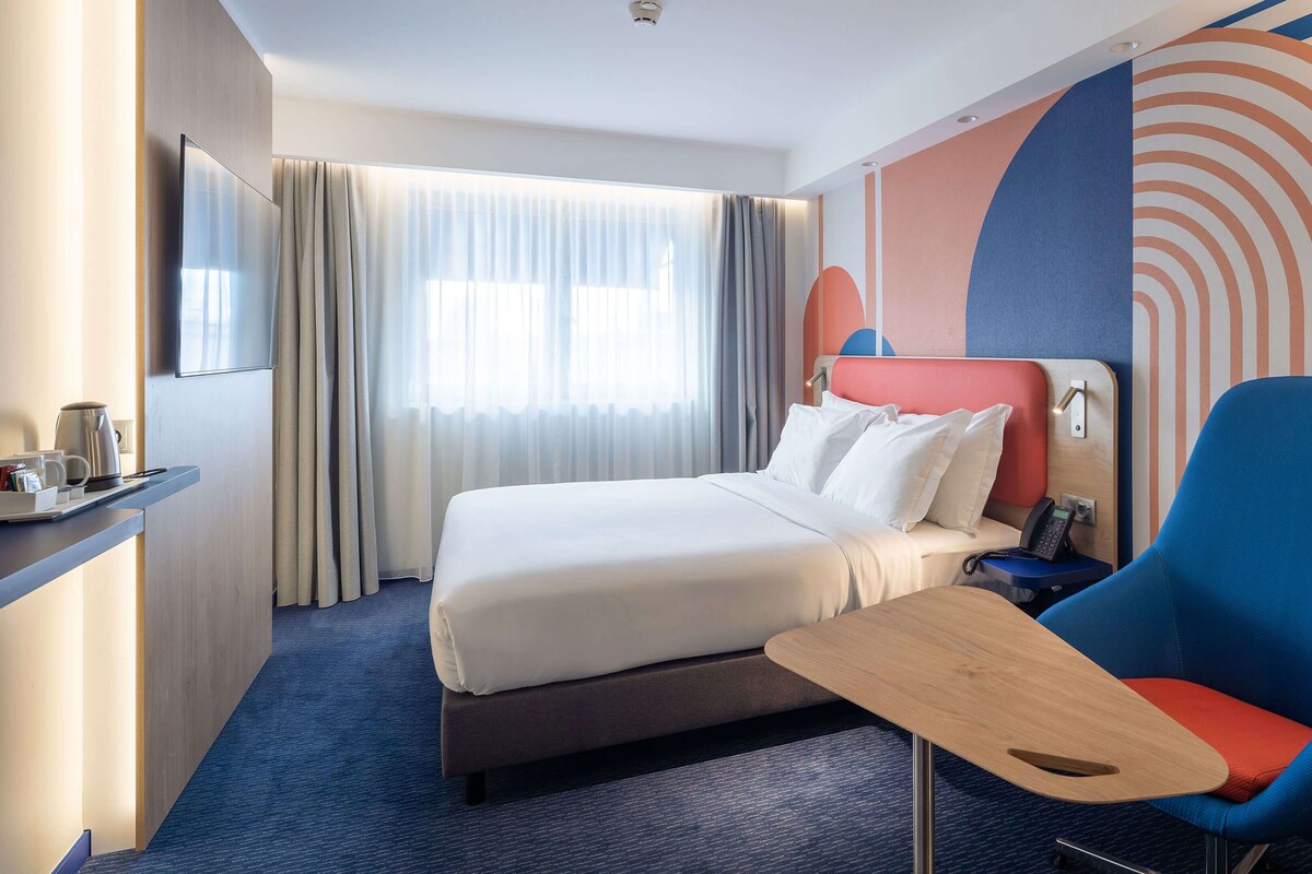 Una habitación de hotel con una cama, una silla, un escritorio y un teléfono, y un televisor.