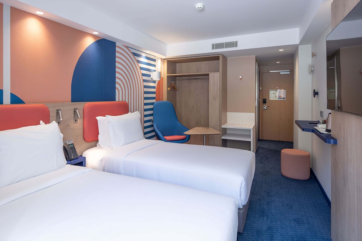 Habitación de hotel con dos camas, un escritorio, una silla y un armario.