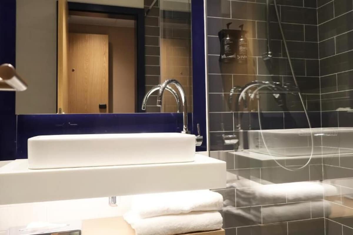 Un baño moderno con ducha de vidrio, lavamanos blanco y espejo sobre él.
