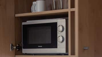 A FRASA microwave in a wooden cabinet with a shelf above containing a white mug and a clear glass.