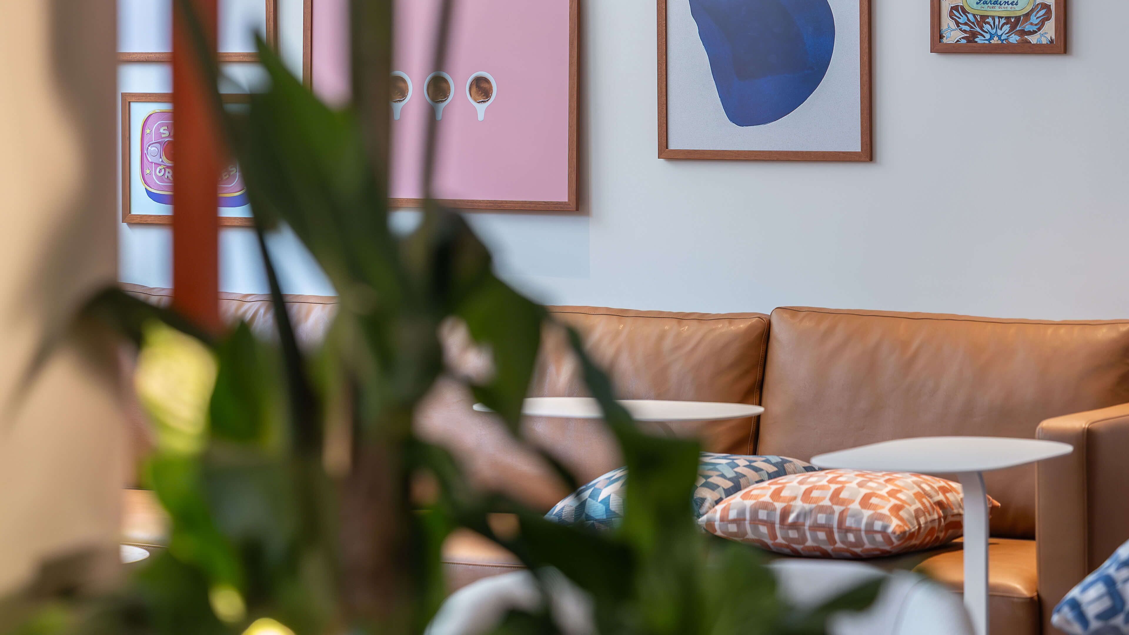 Una habitación con un sofá de cuero marrón, dos mesitas redondas y cojines estampados.