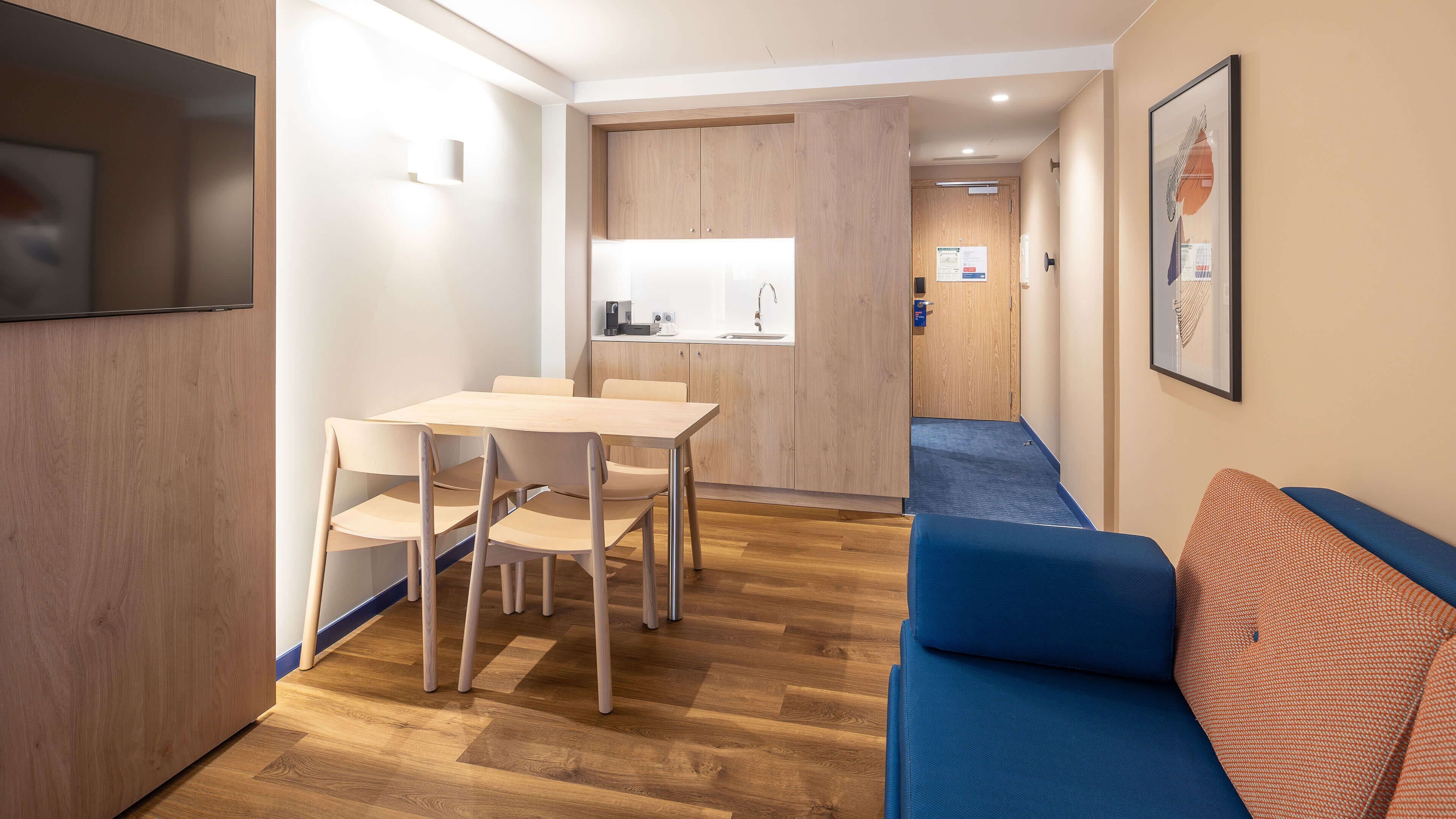 A compact hotel room with a kitchenette, a dining area, and a living space with a sofa.