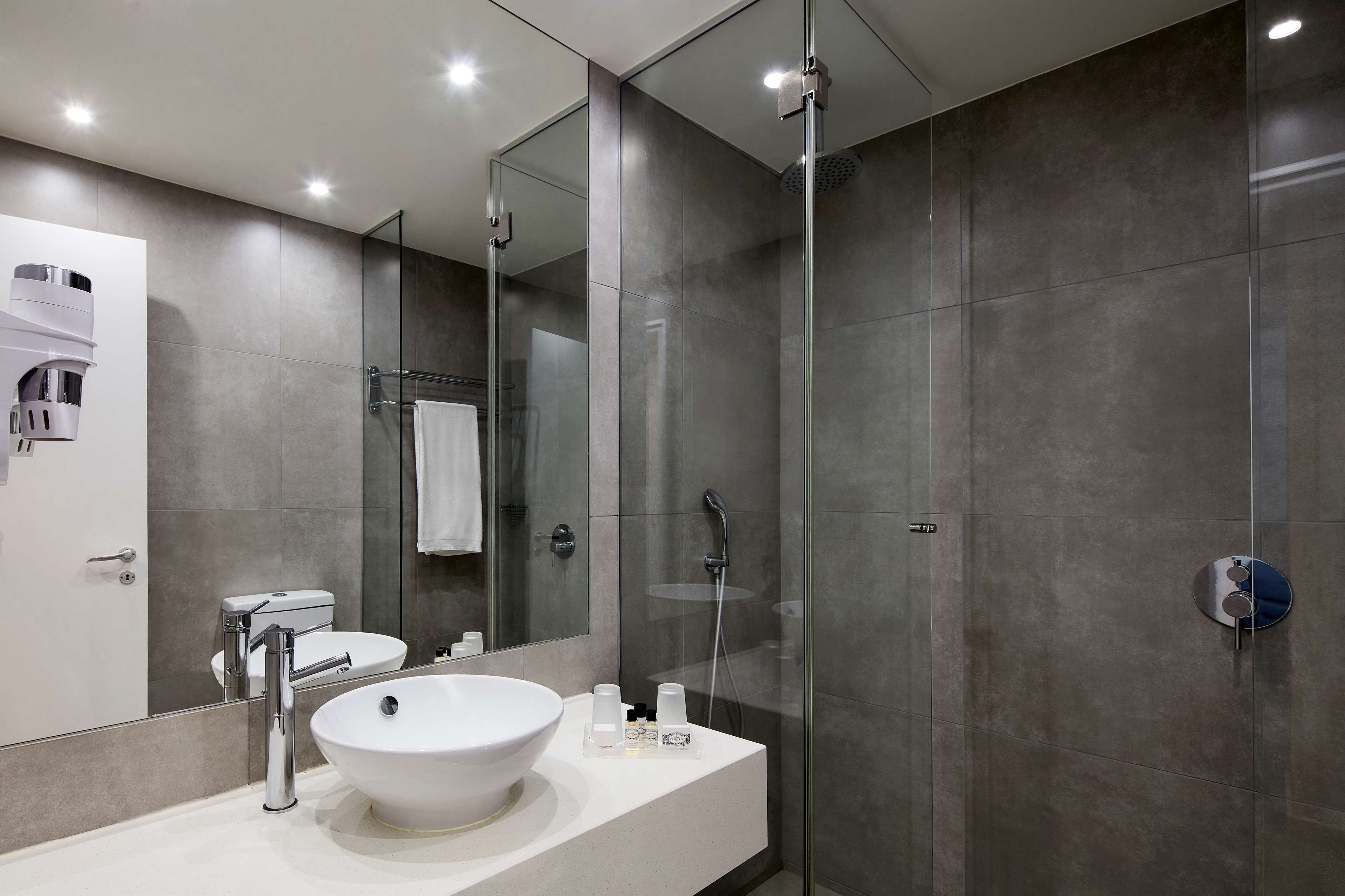A modern bathroom with a large mirror, a white sink, a glass-enclosed shower, and a toilet.