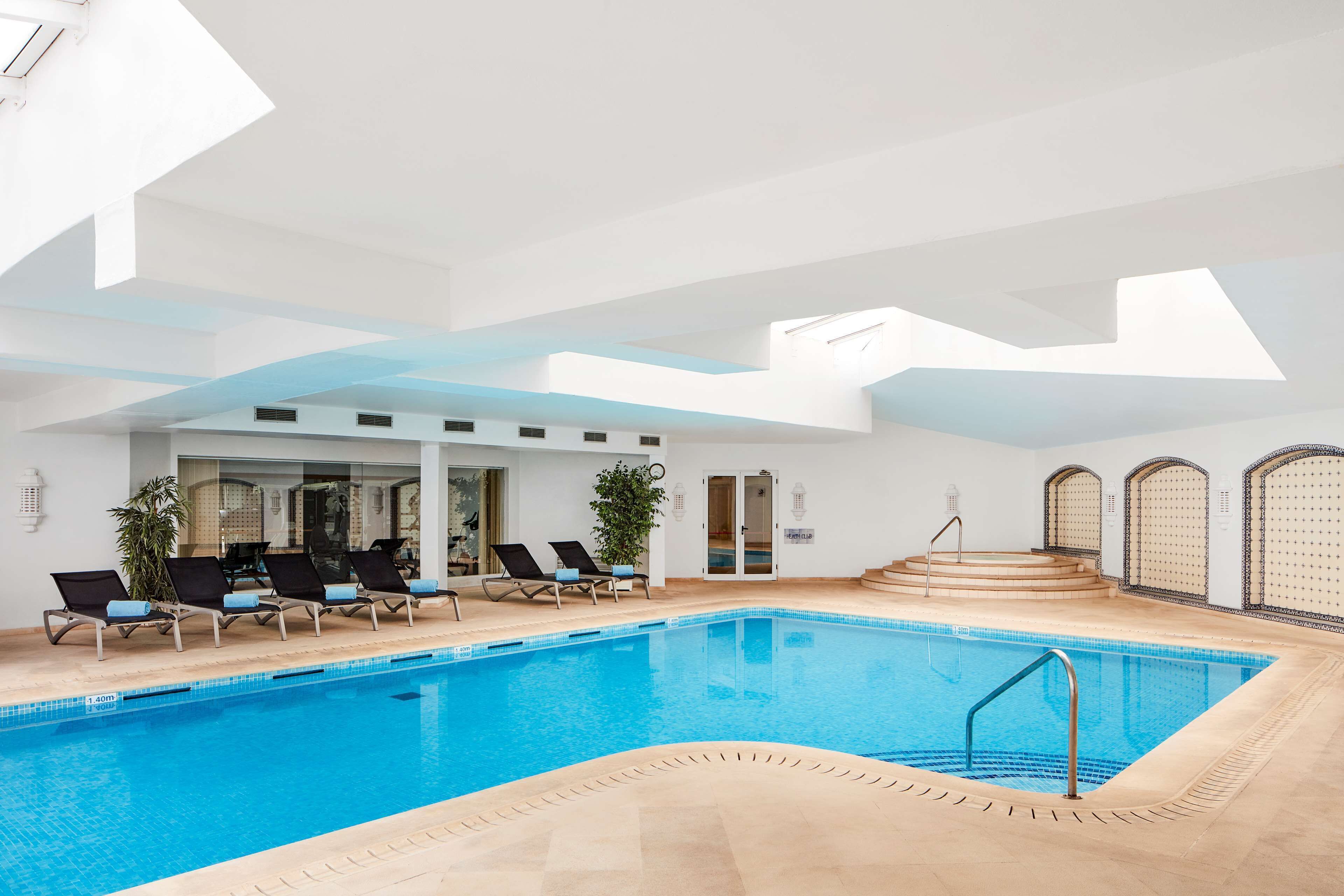 An indoor swimming pool with lounge chairs, a staircase, and a skylight.