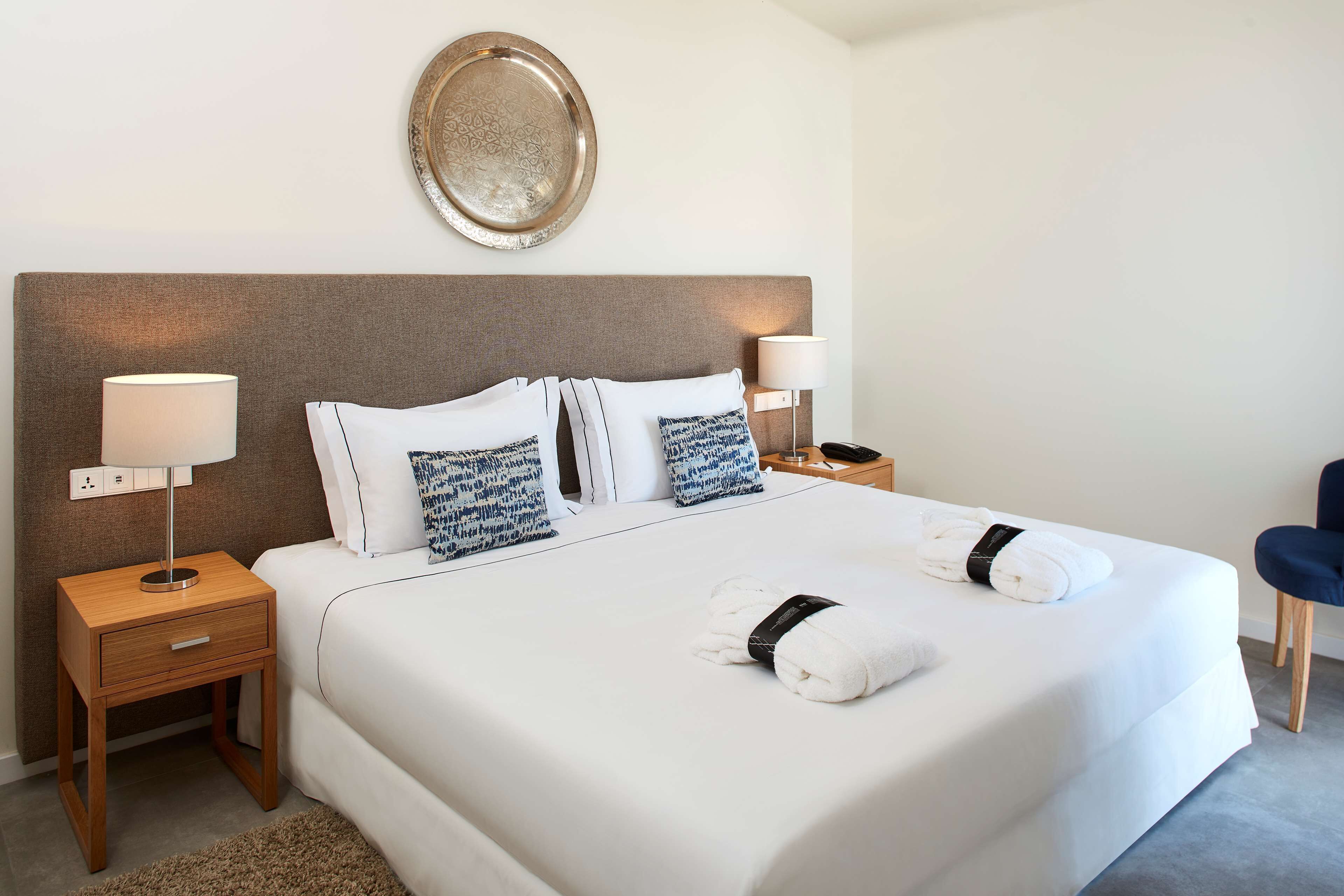 Une chambre d’hôtel avec un grand lit, deux tables de chevet, un plateau fixé au mur et une chaise.