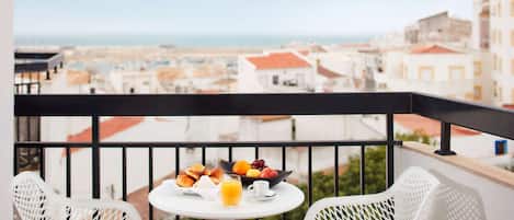 A balcony with a table set for breakfast, two white chairs, and a view of the city and sea.