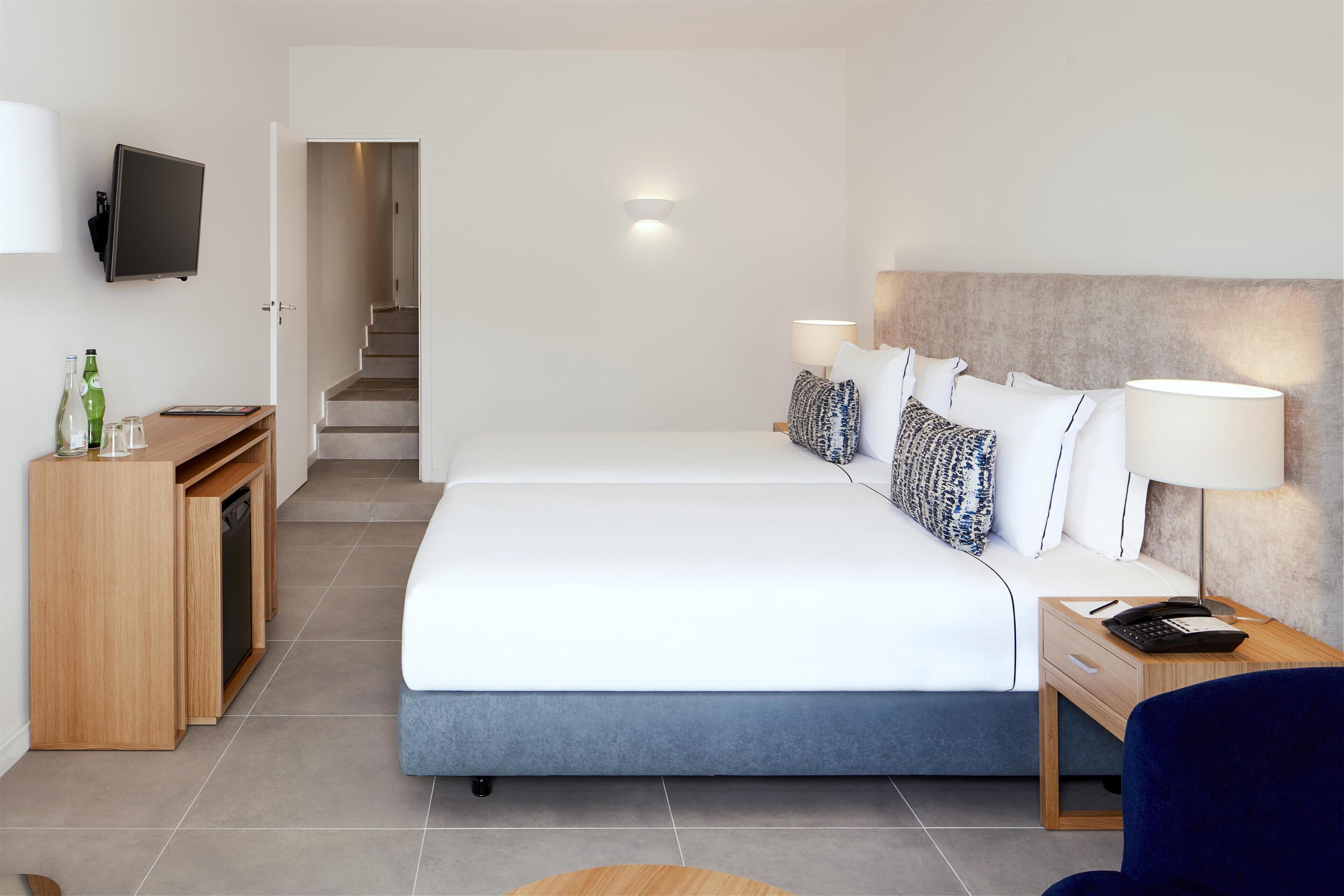A hotel room with a bed, bedside table, lamp, TV, desk with a computer, and a staircase.