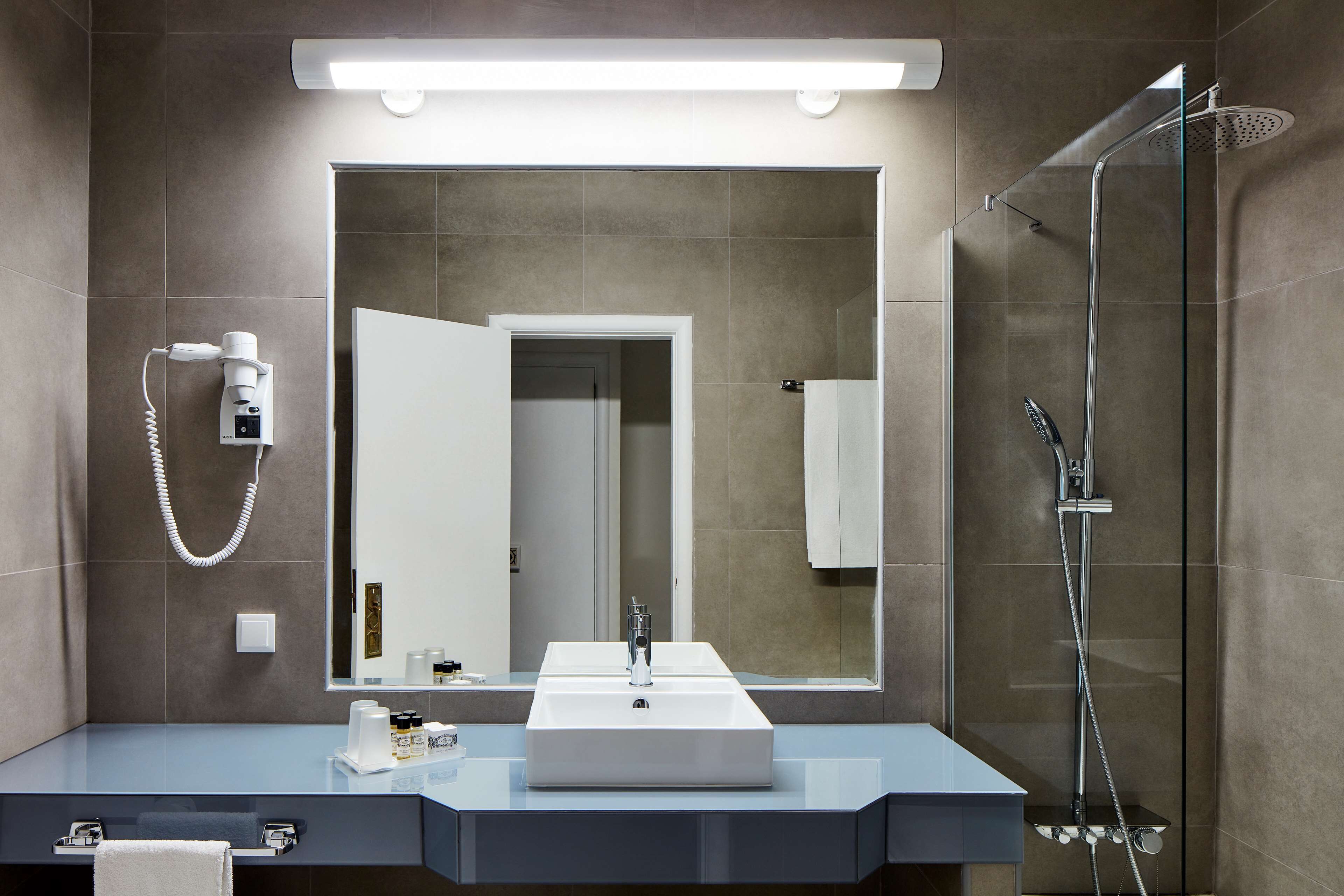 Un baño moderno con un espejo grande, un lavamanos, una ducha y un secador de pelo.