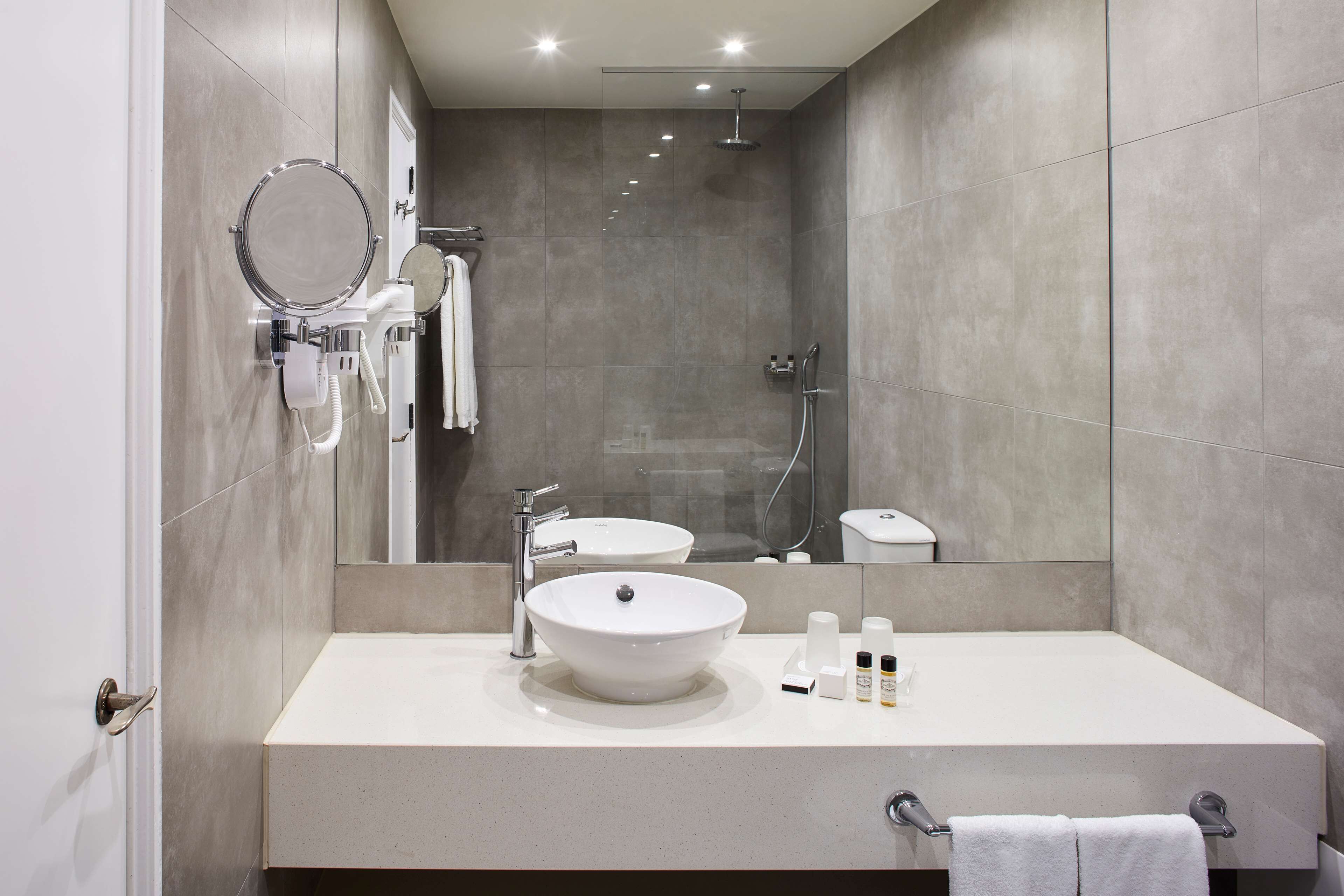 A modern bathroom with a large mirror, a round sink, and a shower.