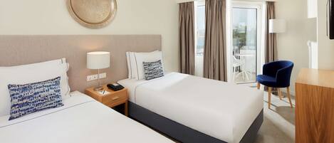 A hotel room with two beds, a desk, a chair, a lamp, and a view of the outdoors.