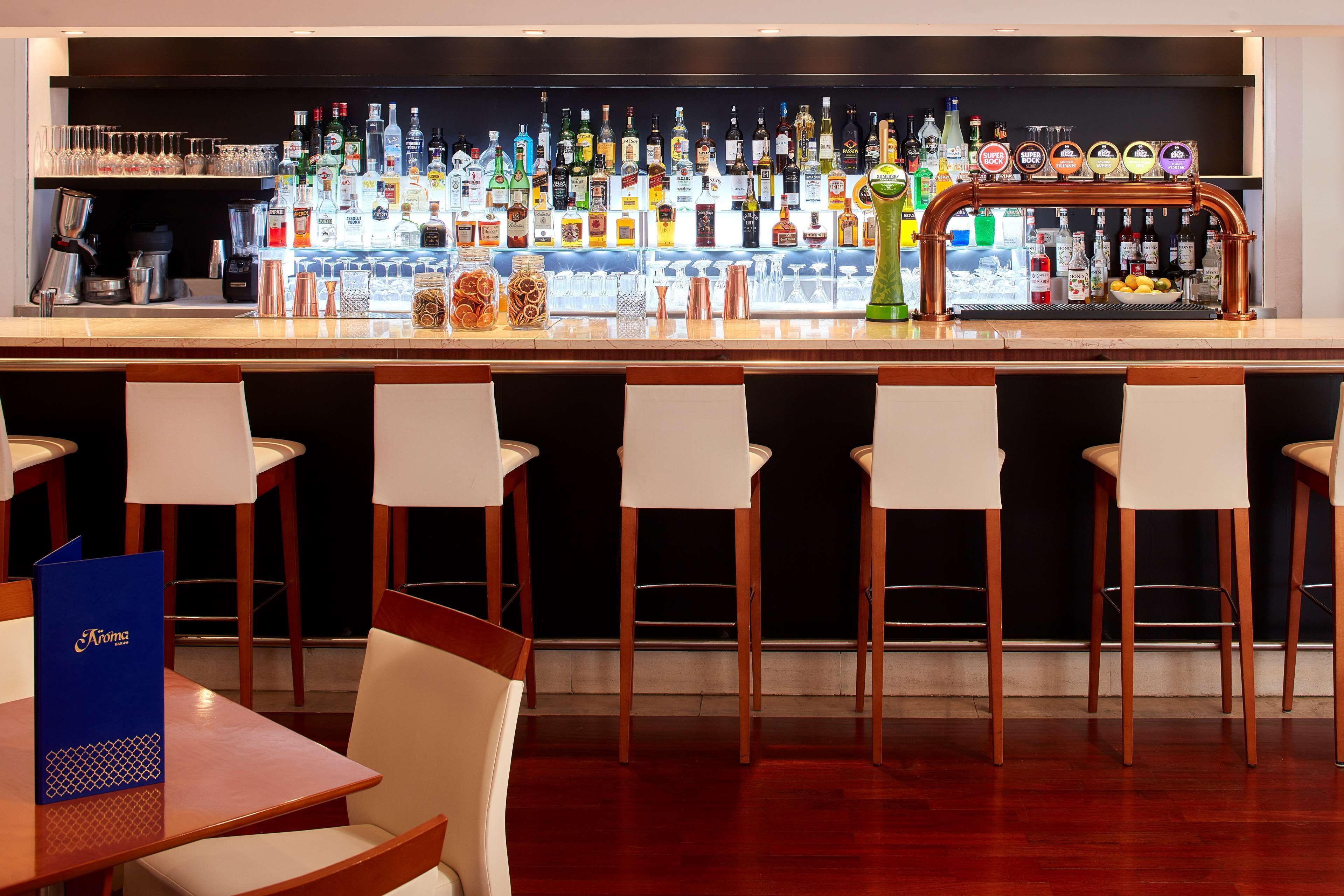 Una zona de bar con varios taburetes, una variedad de botellas de licor y una máquina de café.
