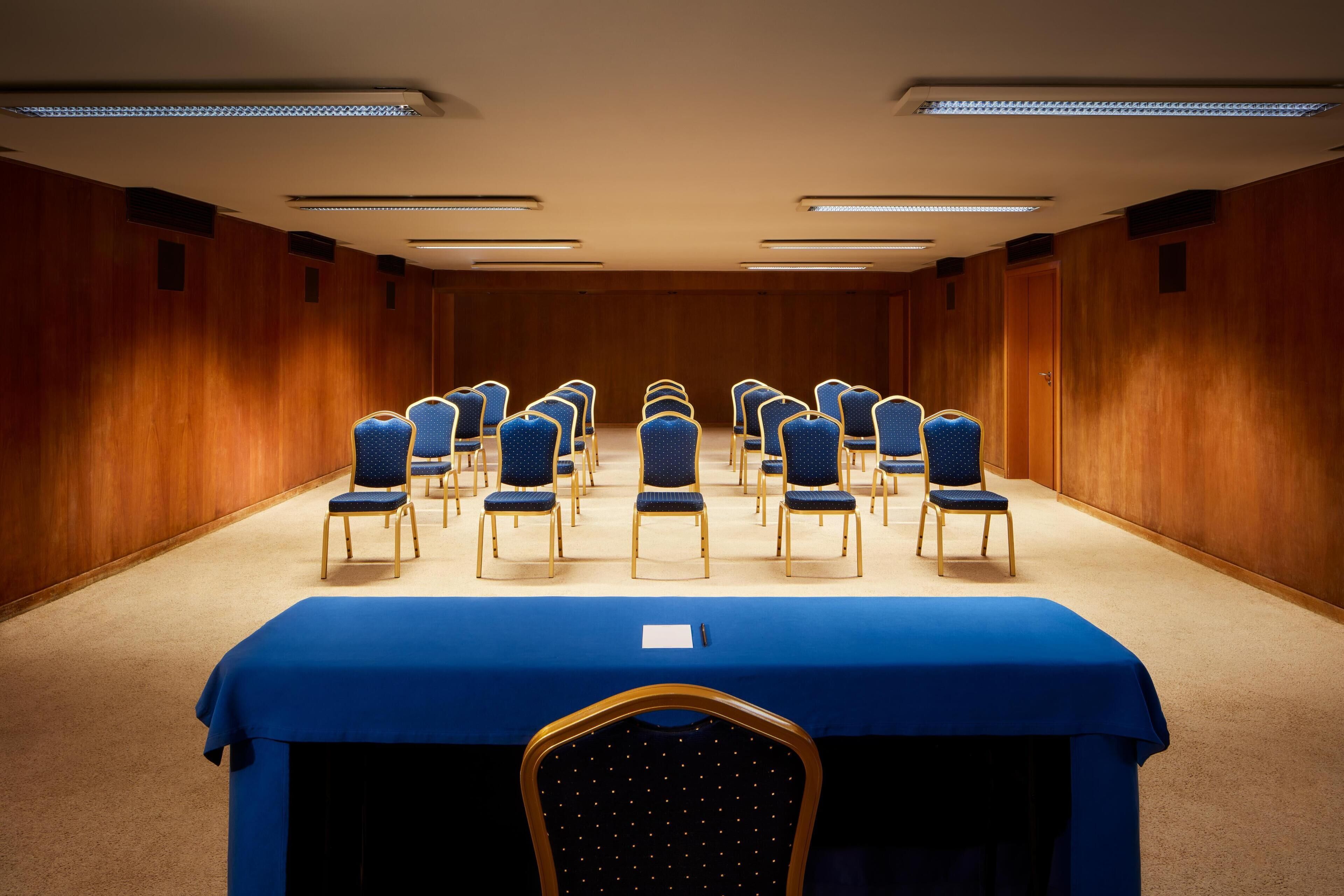 A conference room with rows of chairs, a blue table, and wooden panel walls.