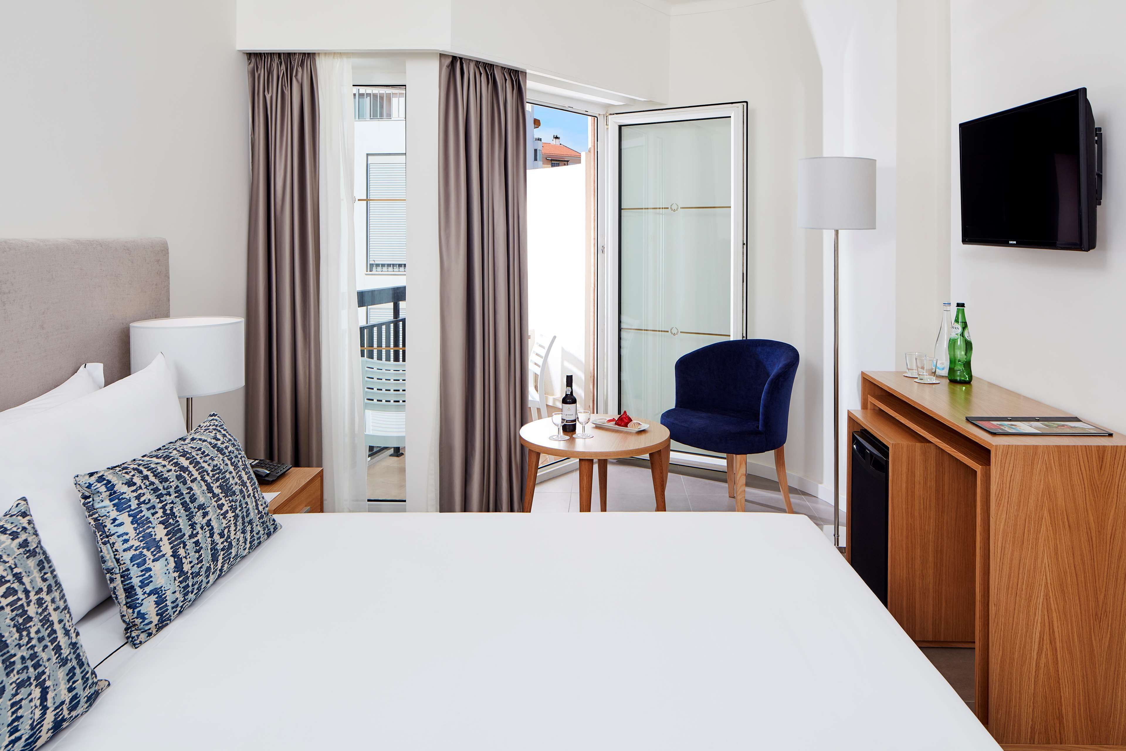 Une chambre d’hôtel avec un lit, un bureau, une chaise, une télévision et un balcon.