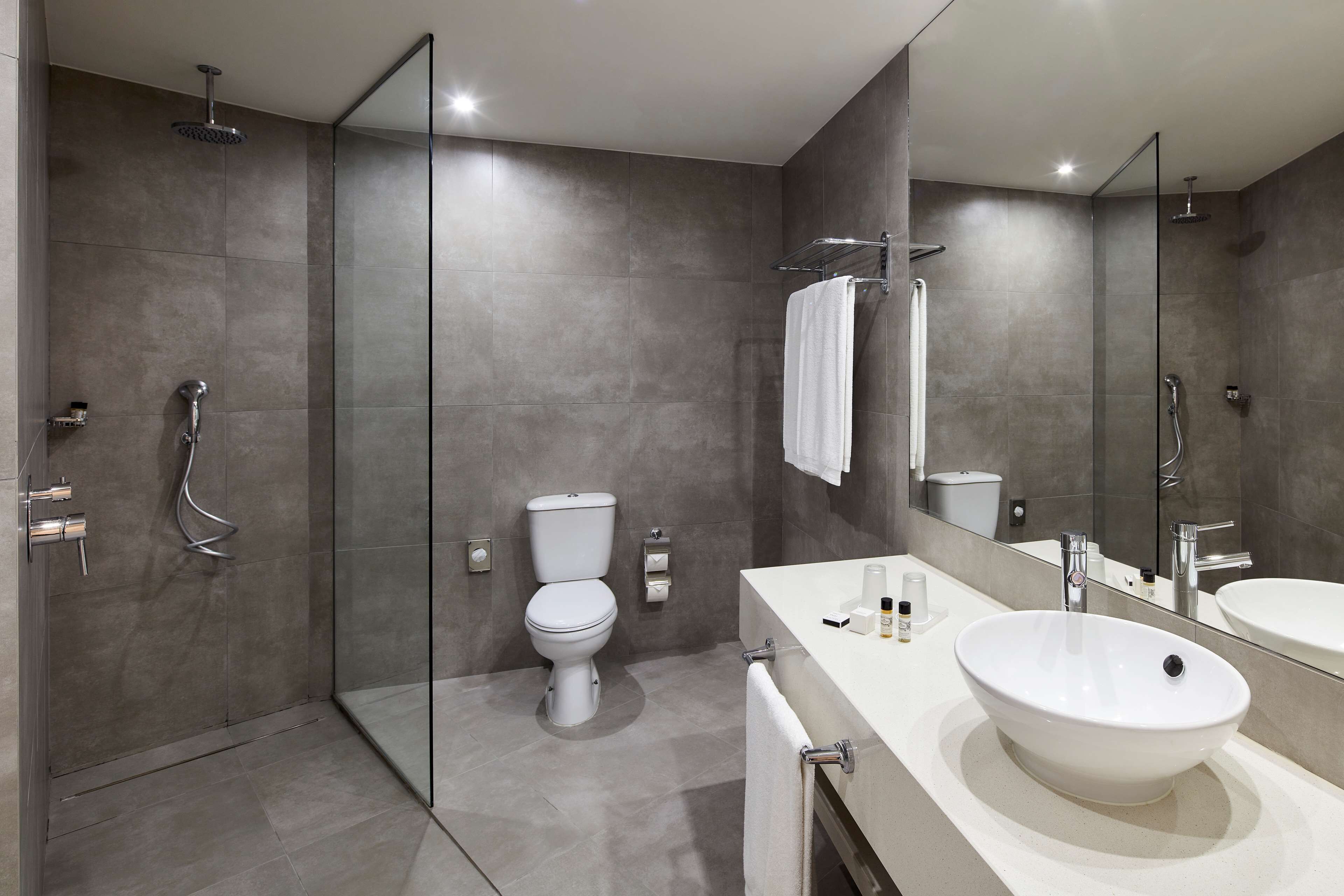 A modern bathroom with a glass shower enclosure, a toilet, a sink with a mirror, and a towel rack.