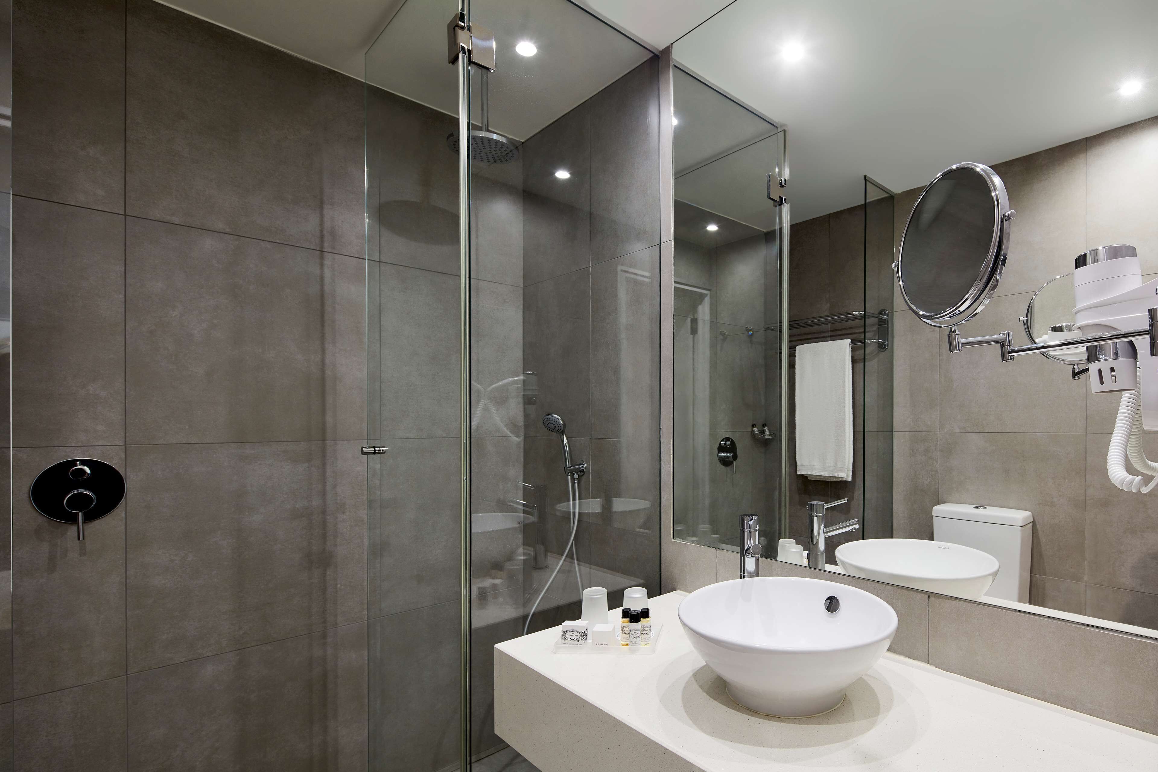 A modern bathroom with a glass-enclosed shower, a white sink, and a large mirror.