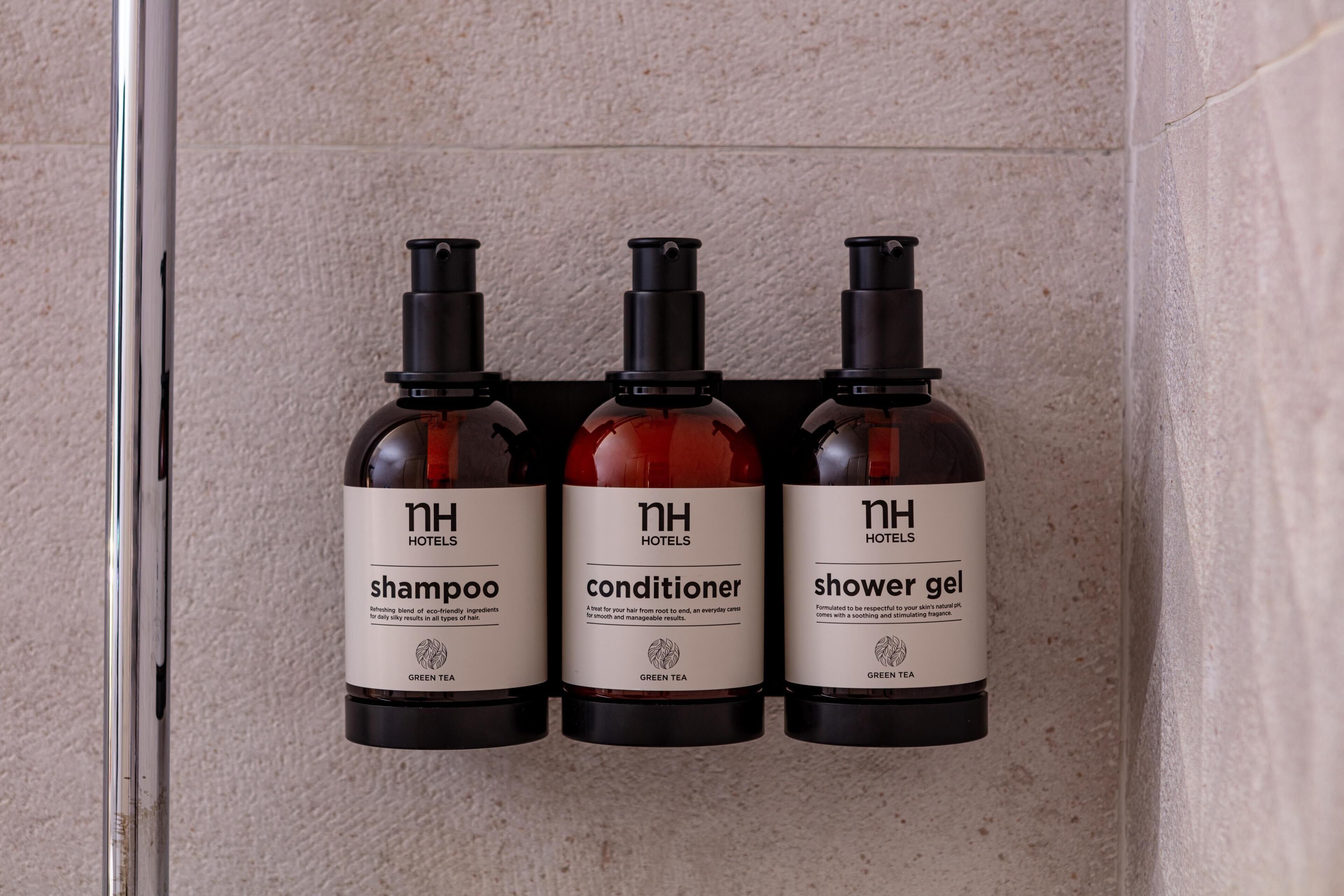Tres botellas de artículos de tocador de hotel: champú, acondicionador y gel de ducha, todas con la etiqueta 'nh hotels' y 'té verde'.
