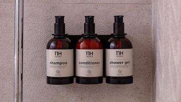 Three bottles of hotel amenities: shampoo, conditioner, and shower gel, all labeled with 'nh hotels' and 'green tea'.