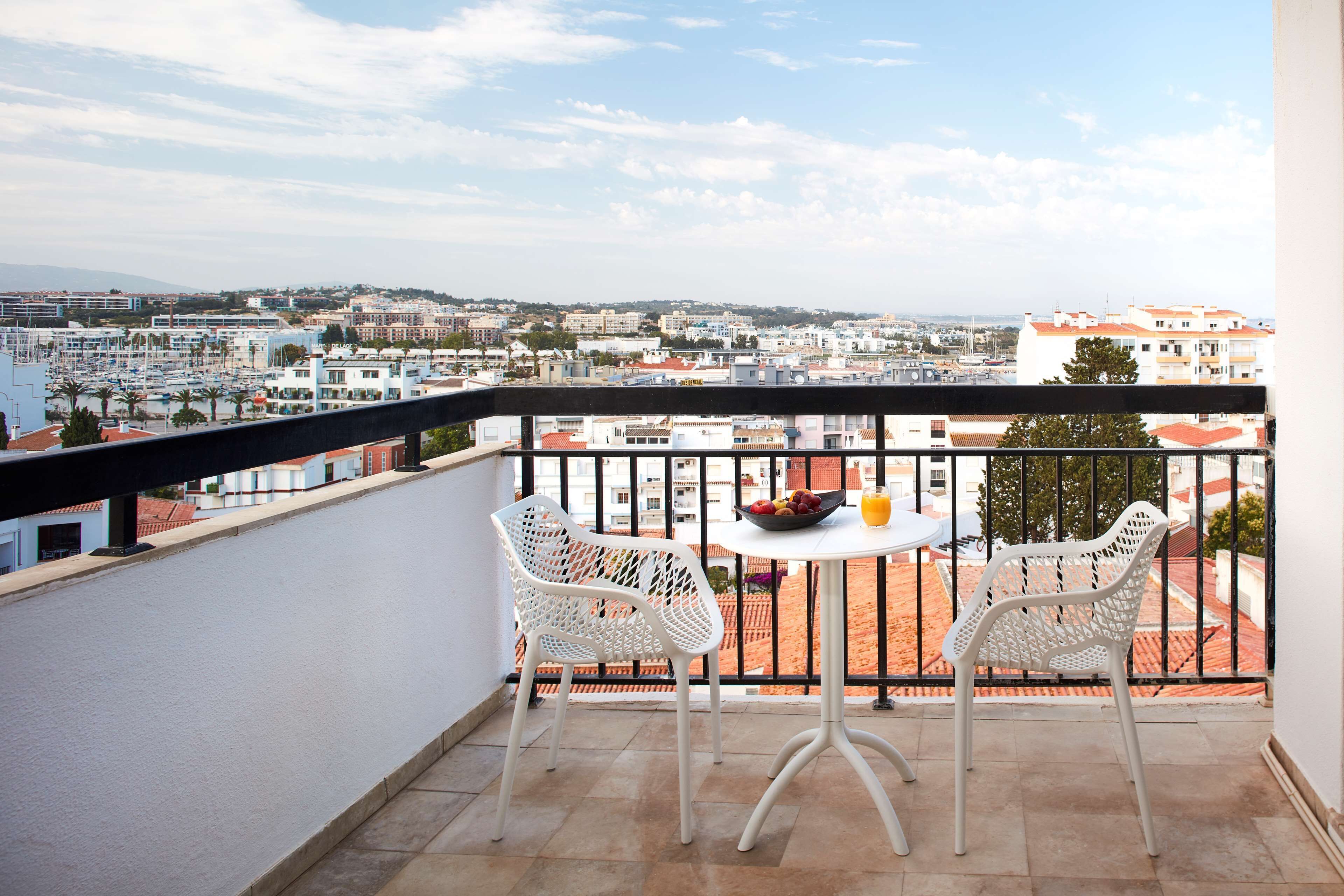 A balcony with two white chairs, a small table, and a bowl of fruit.