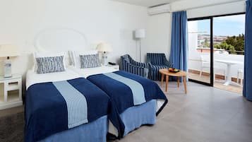 Habitación de hotel con dos camas, balcón, comedor y vistas a la ciudad.