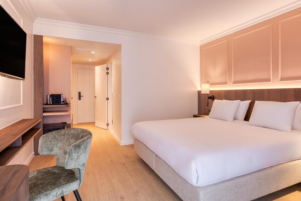 A hotel room with a large bed, a desk with a chair, a TV, and a wooden shelf.