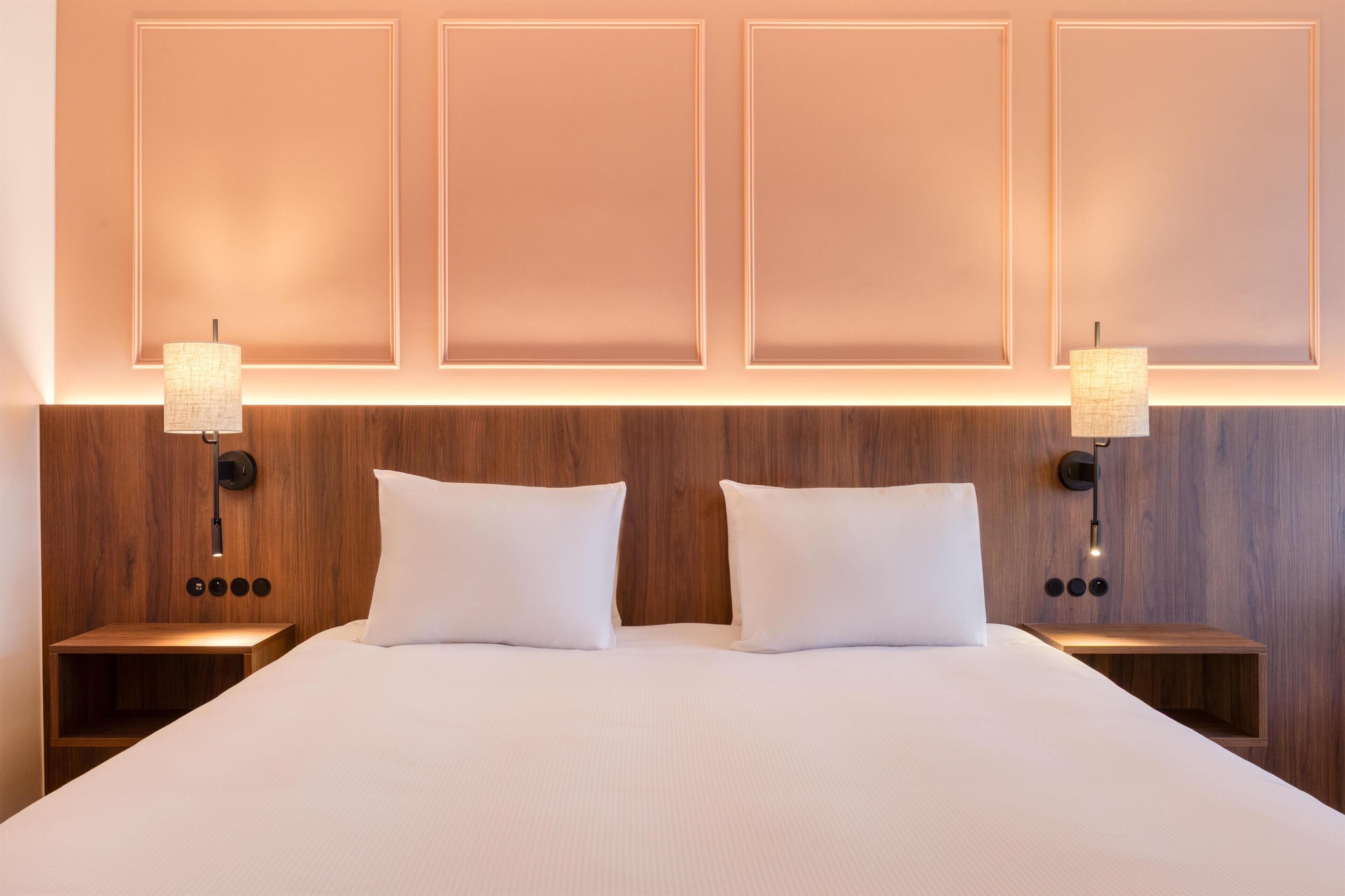 Une chambre d’hôtel avec un grand lit, deux tables de chevet avec des lampes et une tête de lit en bois.