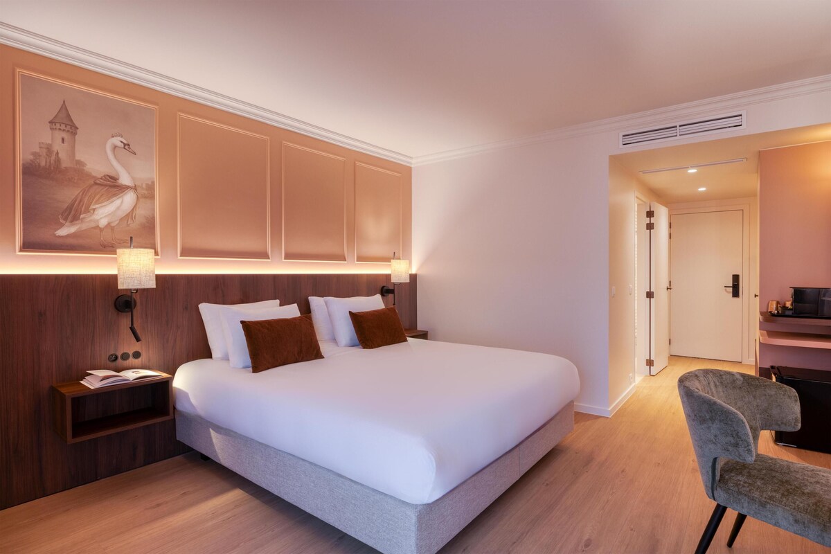 A hotel room with a large bed, a nightstand, a desk, and a chair.