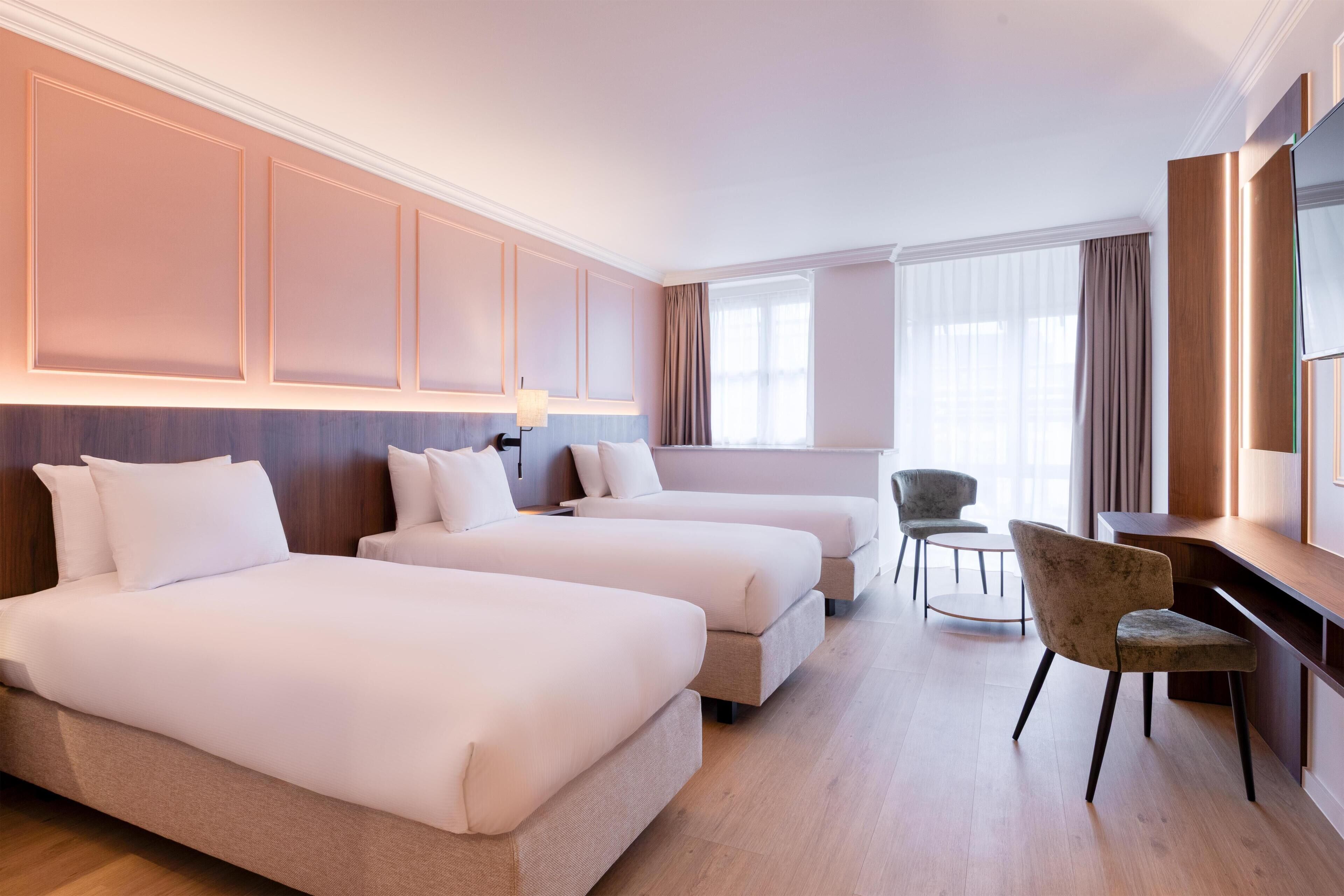 Een hotelkamer met twee bedden, een bureau, een stoel en een groot raam.