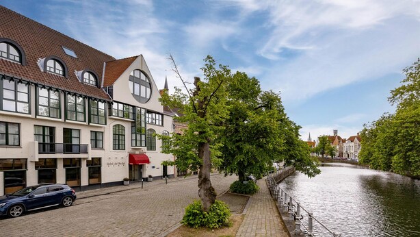 A building with a red awning, a tree in front, and a canal beside it. - Golden Tulip De' Medici Hotel (Bruges)