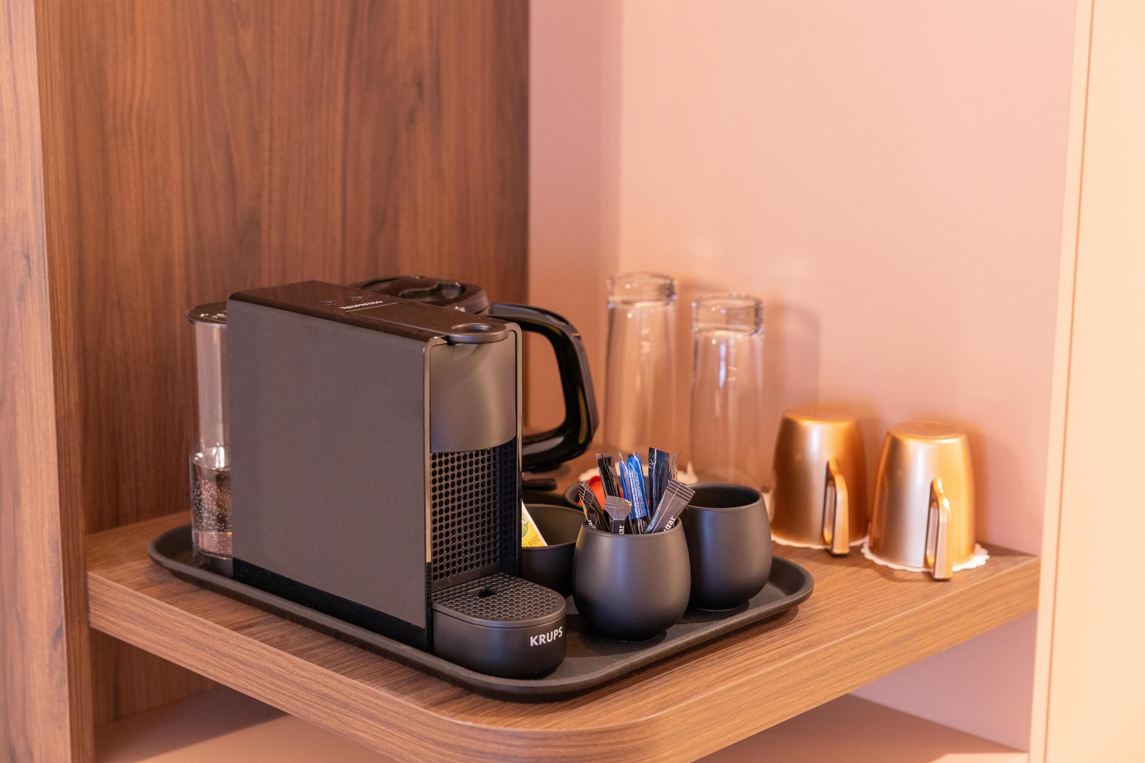 Une machine à café posée sur un plateau, un porte-gobelet avec des ustensiles, et deux bougies sur une étagère.