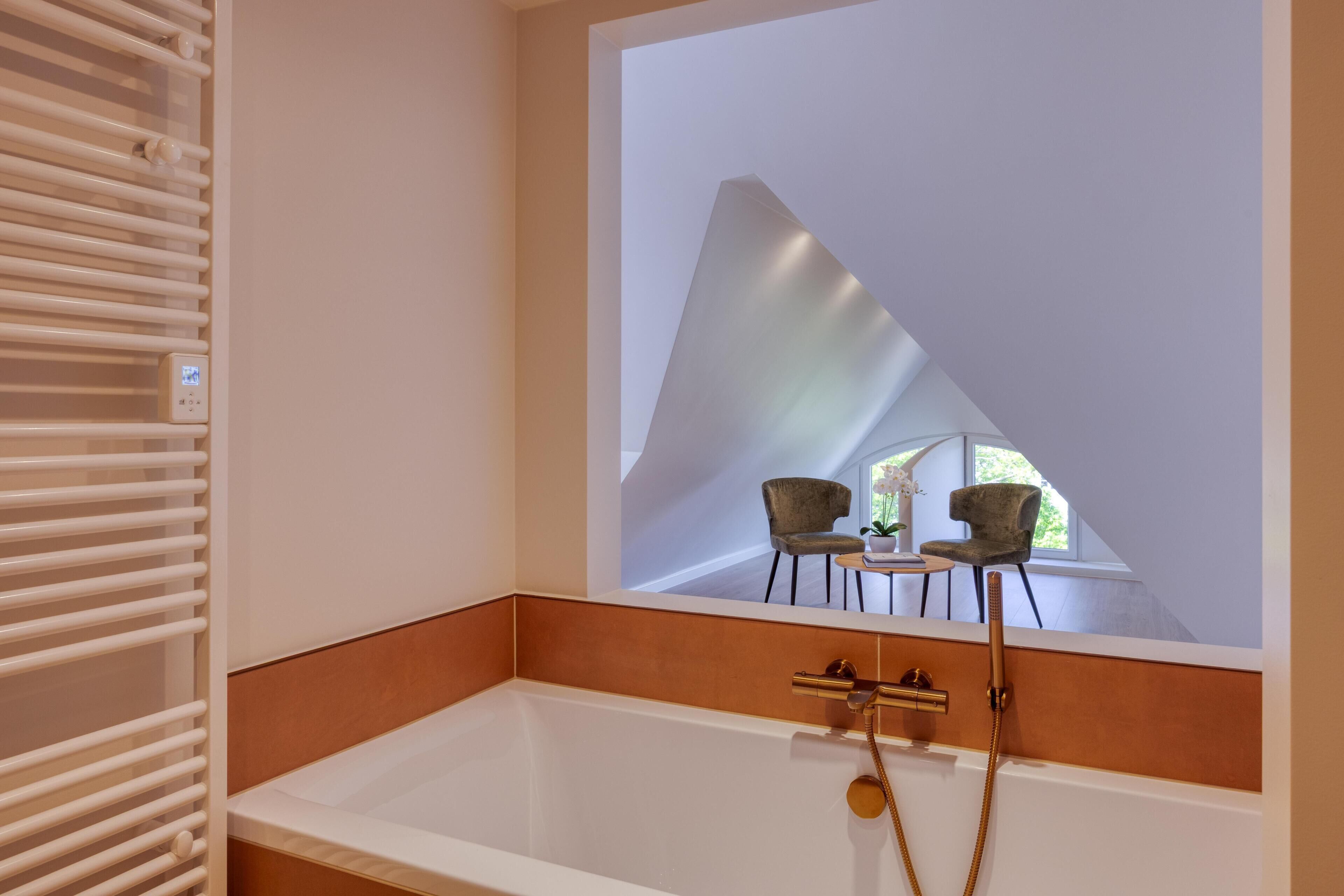 Ein modernes Badezimmer mit einer Badewanne, einem Handtuchhalter und einem Spiegel, der einen Essbereich mit Stühlen und einem Tisch reflektiert.