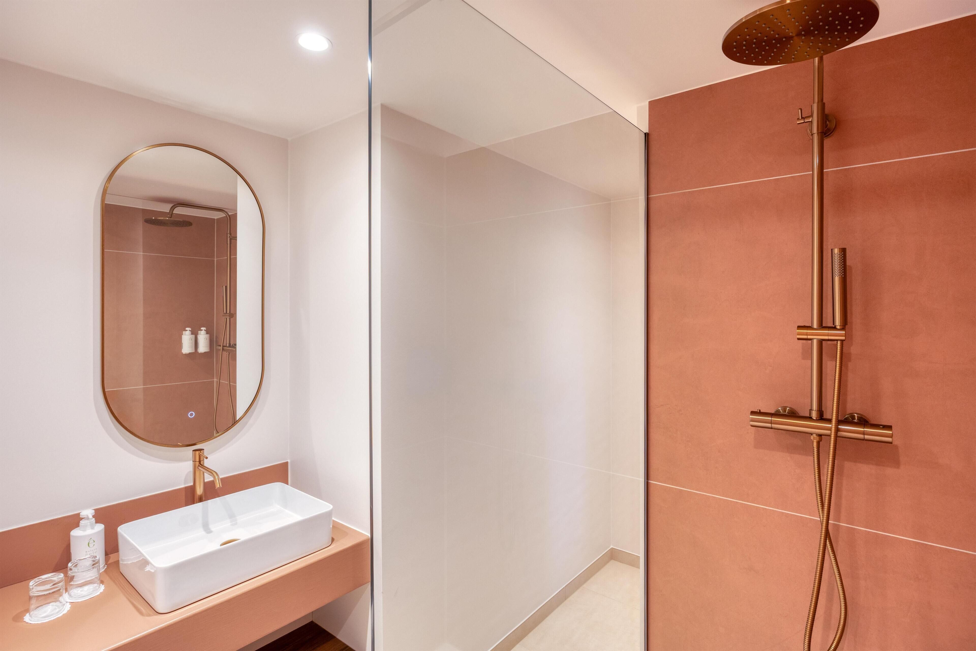 A modern bathroom with a rectangular sink, a round mirror, and a shower with a handheld showerhead.