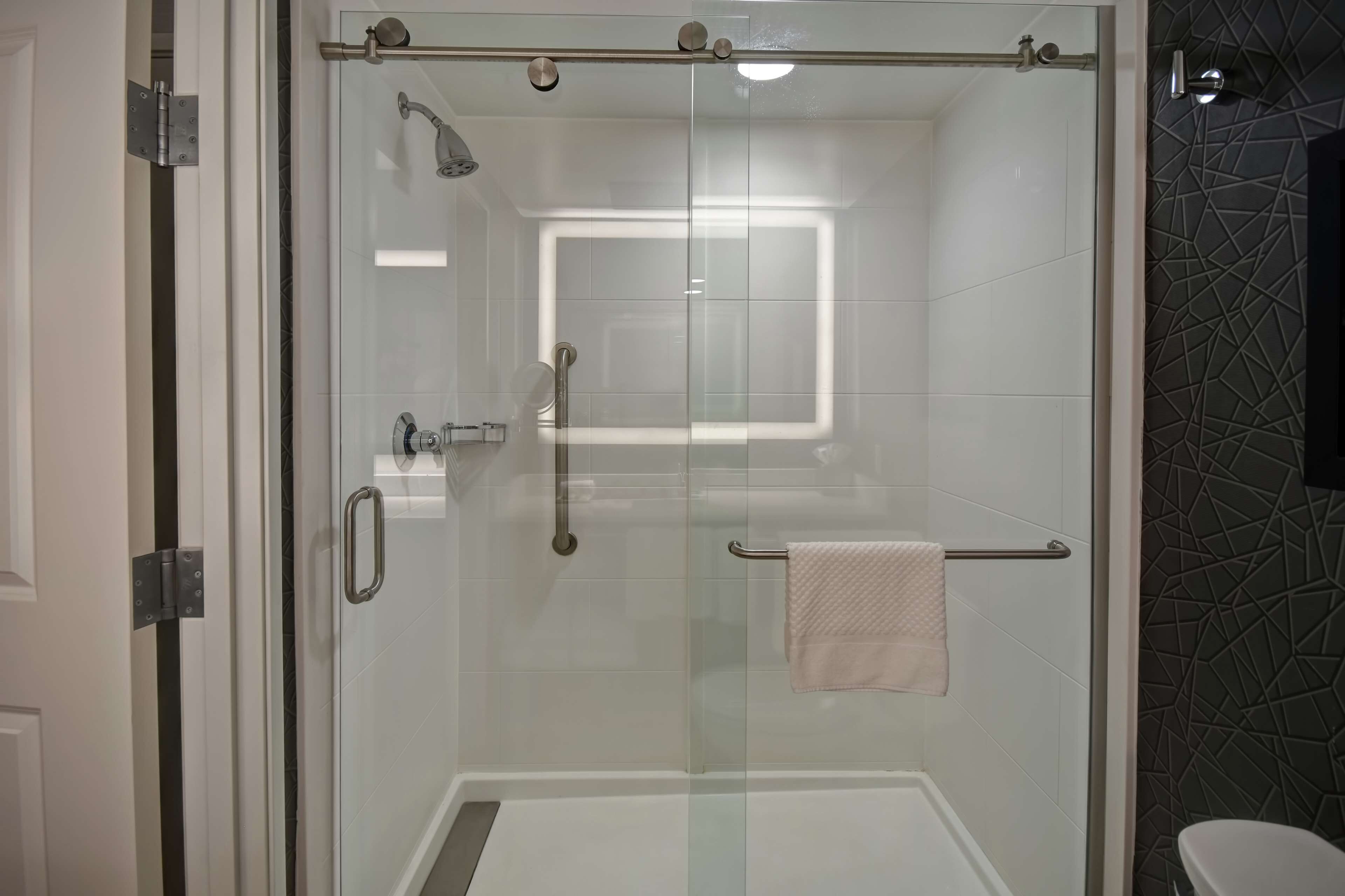 A glass-enclosed shower with a handrail, a towel rack, and a visible window.