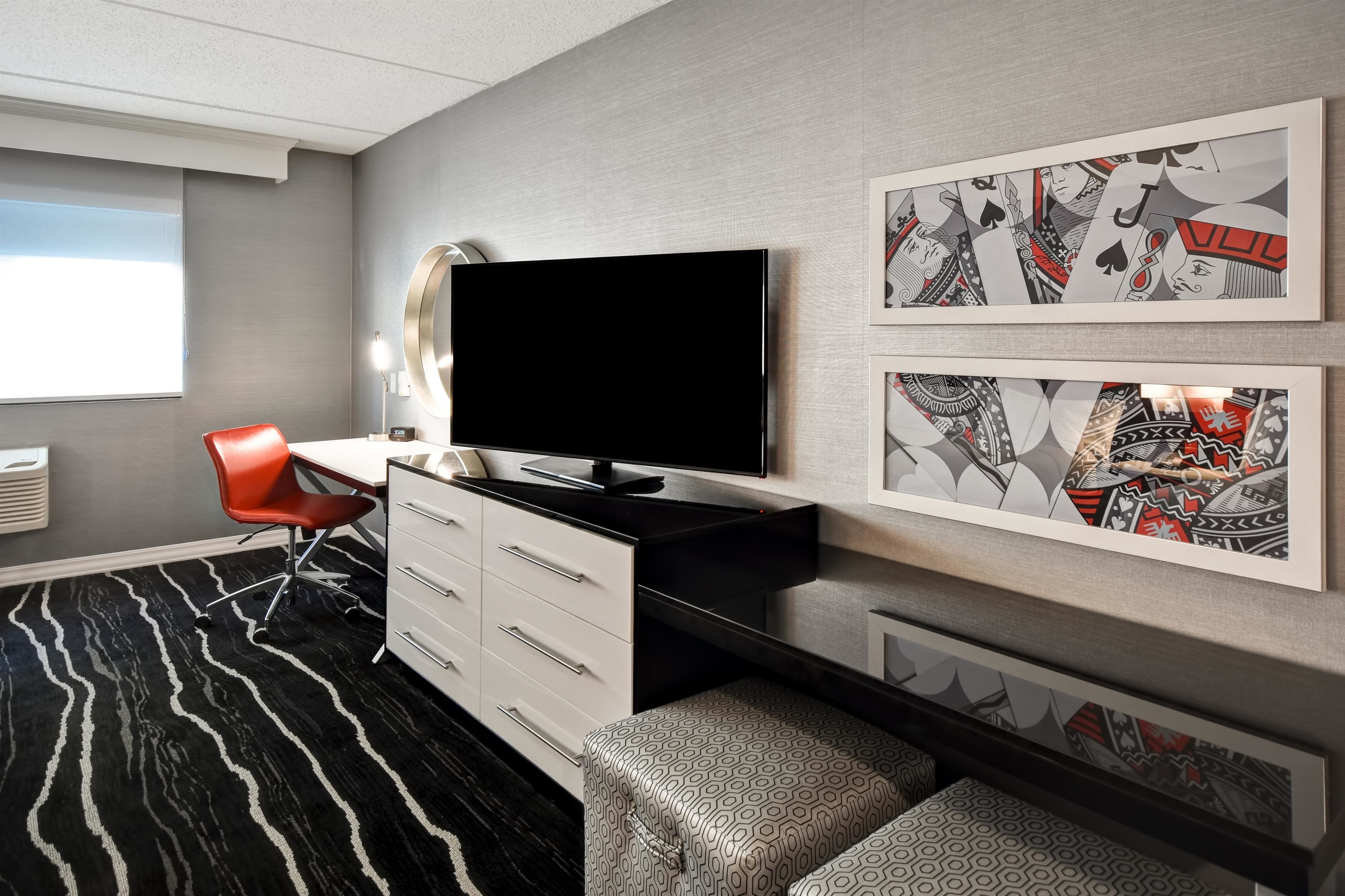 Een moderne hotelkamer met een flatscreen televisie, een rode stoel, een witte kapstok en kunstwerken met een patroon op de muren.